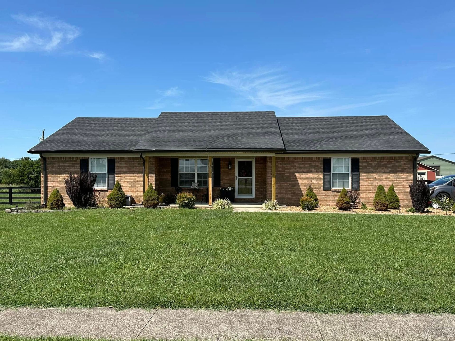 A brick house with a black roof is sitting on top of a lush green field.