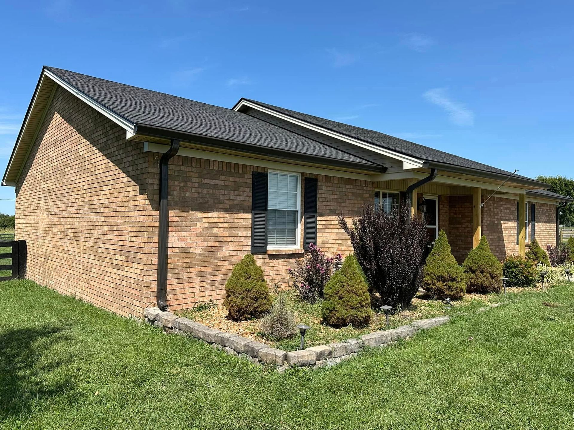 A brick house with a black roof is sitting on top of a lush green field.