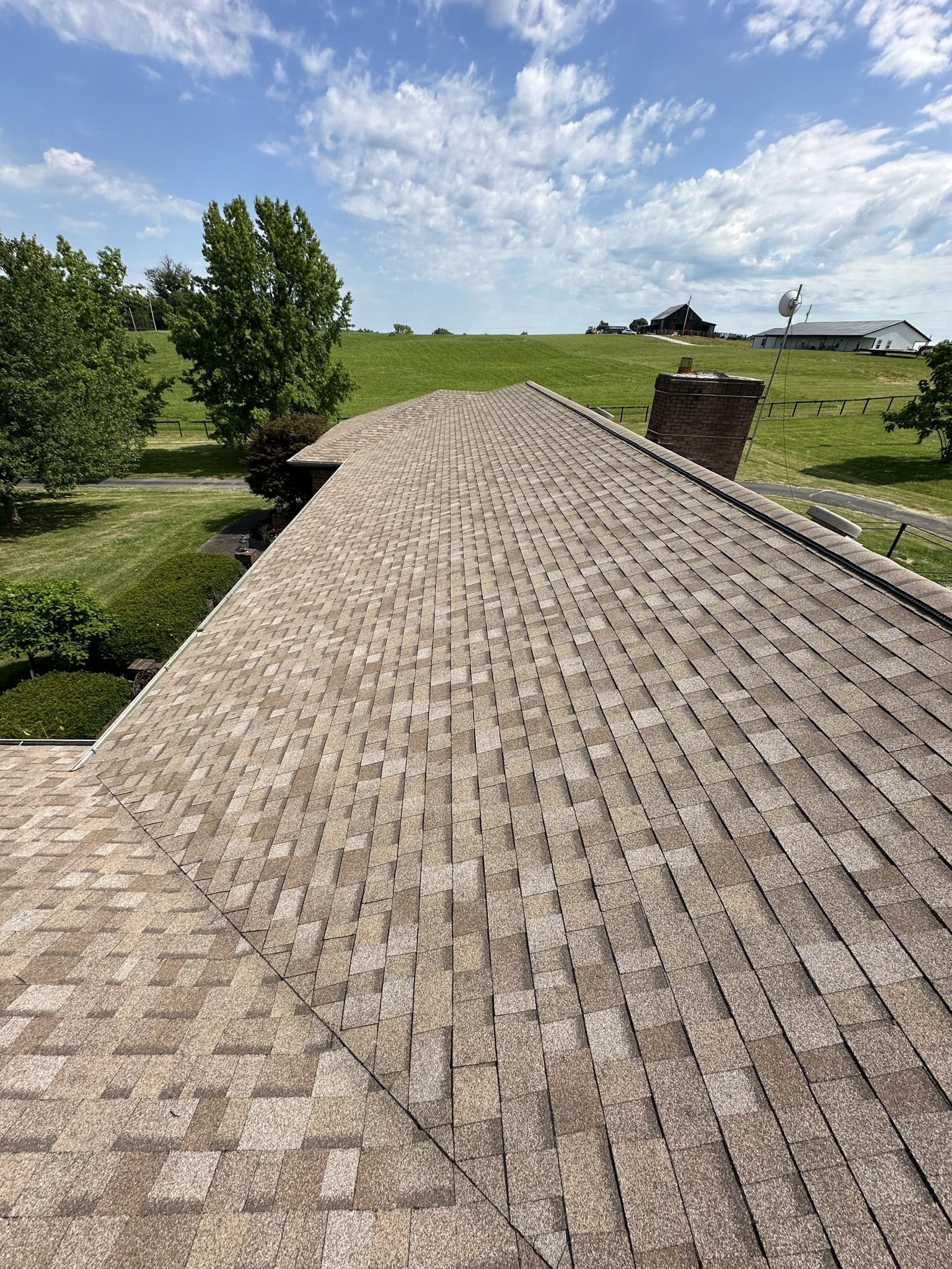 A roof of a house with a chimney and a field in the background.