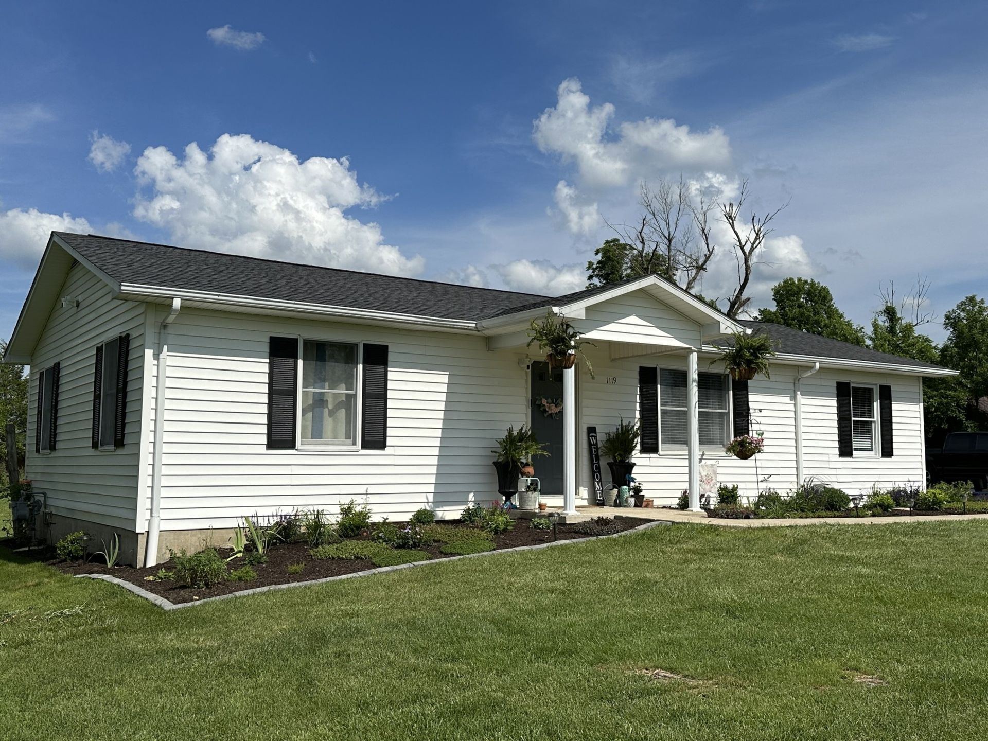 A white house with black shutters is sitting on top of a lush green field.