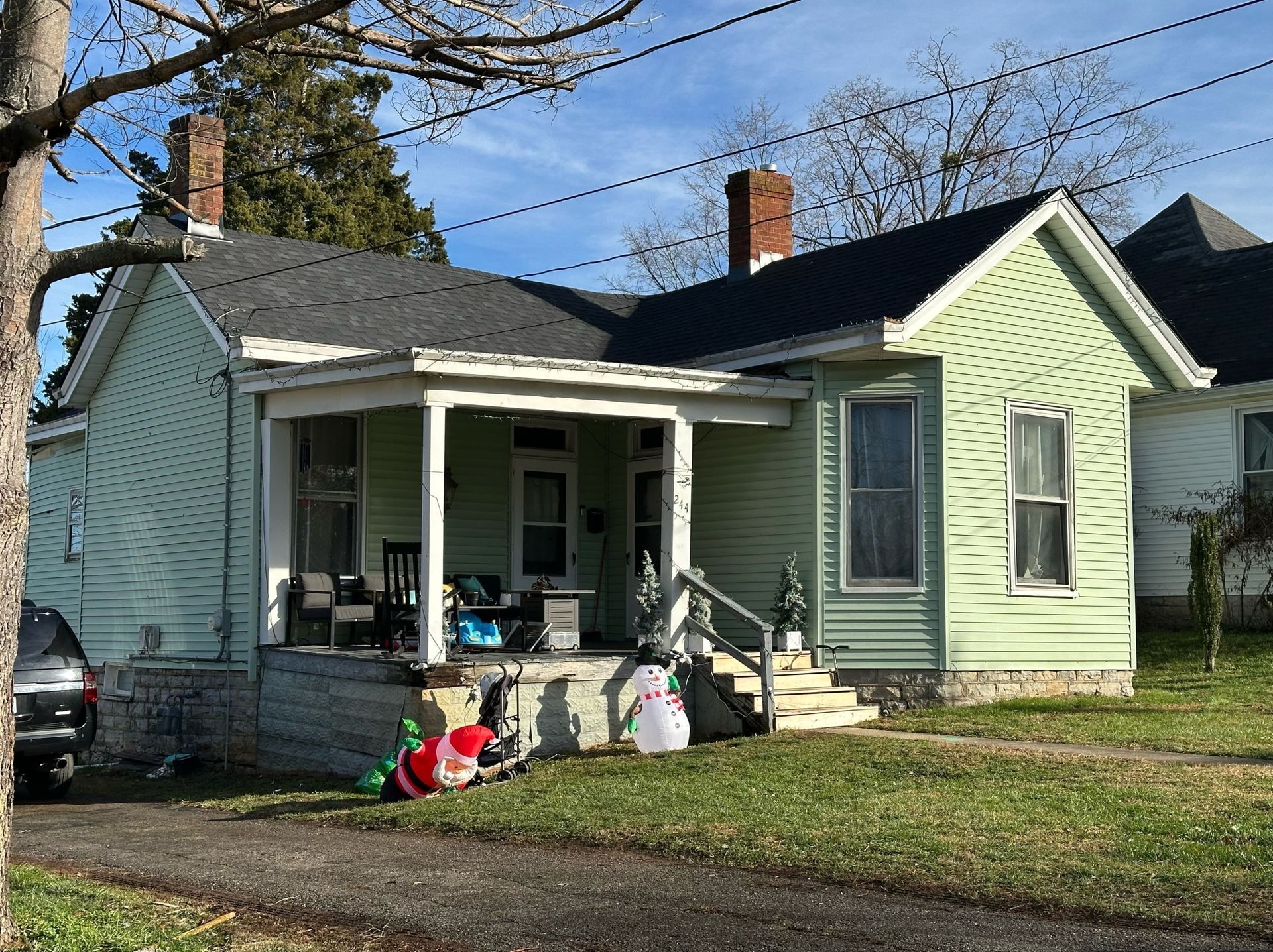 A small green house with a porch and a car parked in front of it.