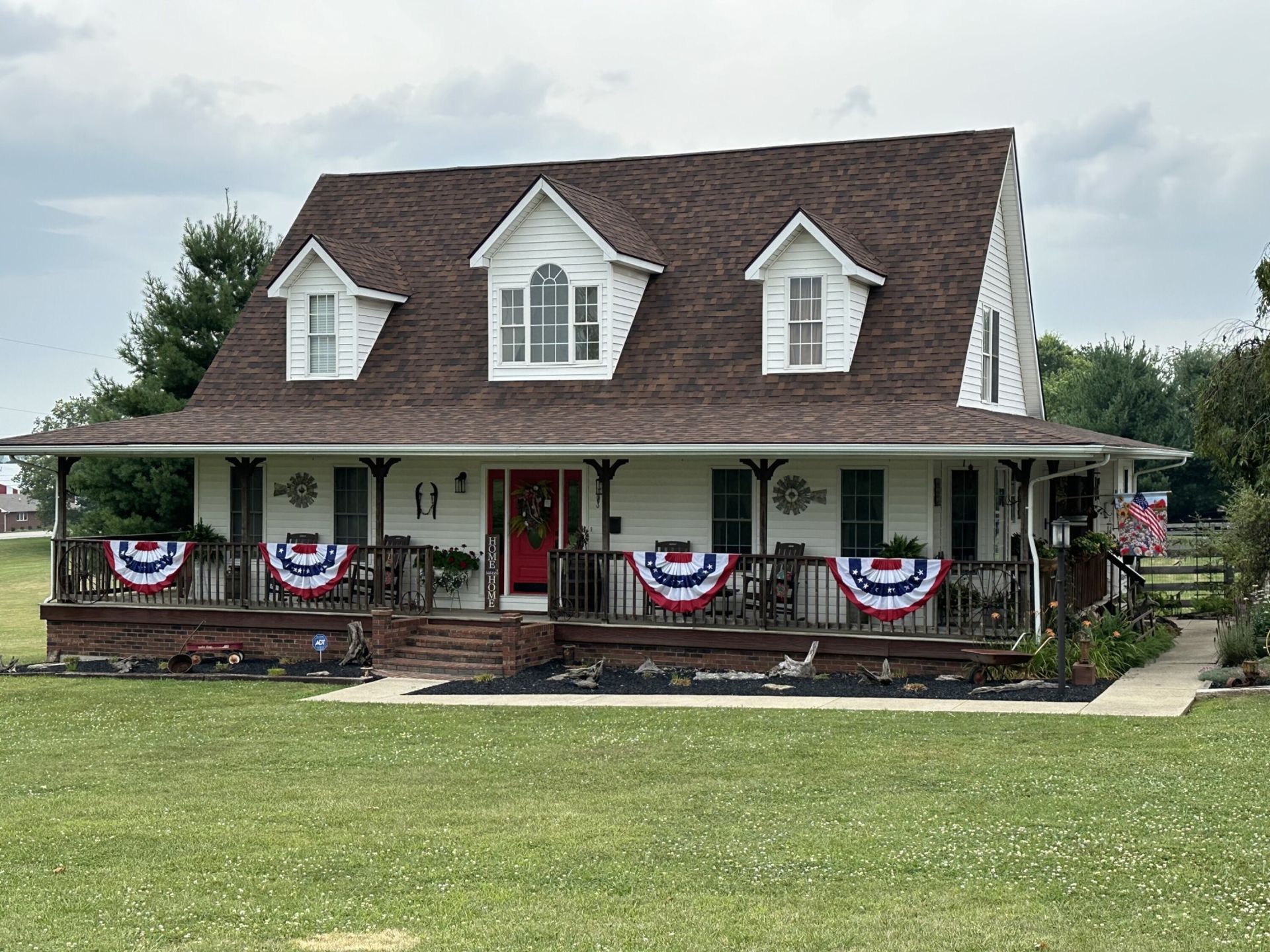 A large white house with a porch decorated for the fourth of july.