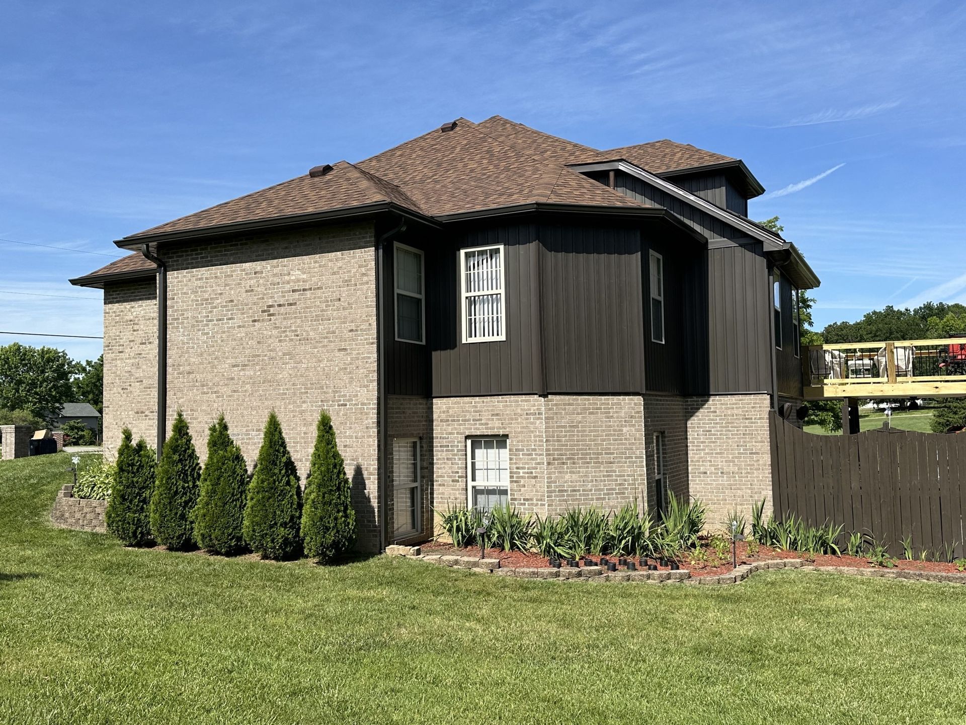 A large brick house with a brown roof is sitting on top of a lush green field.