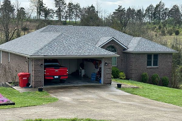 A red truck is parked in the garage of a brick house.