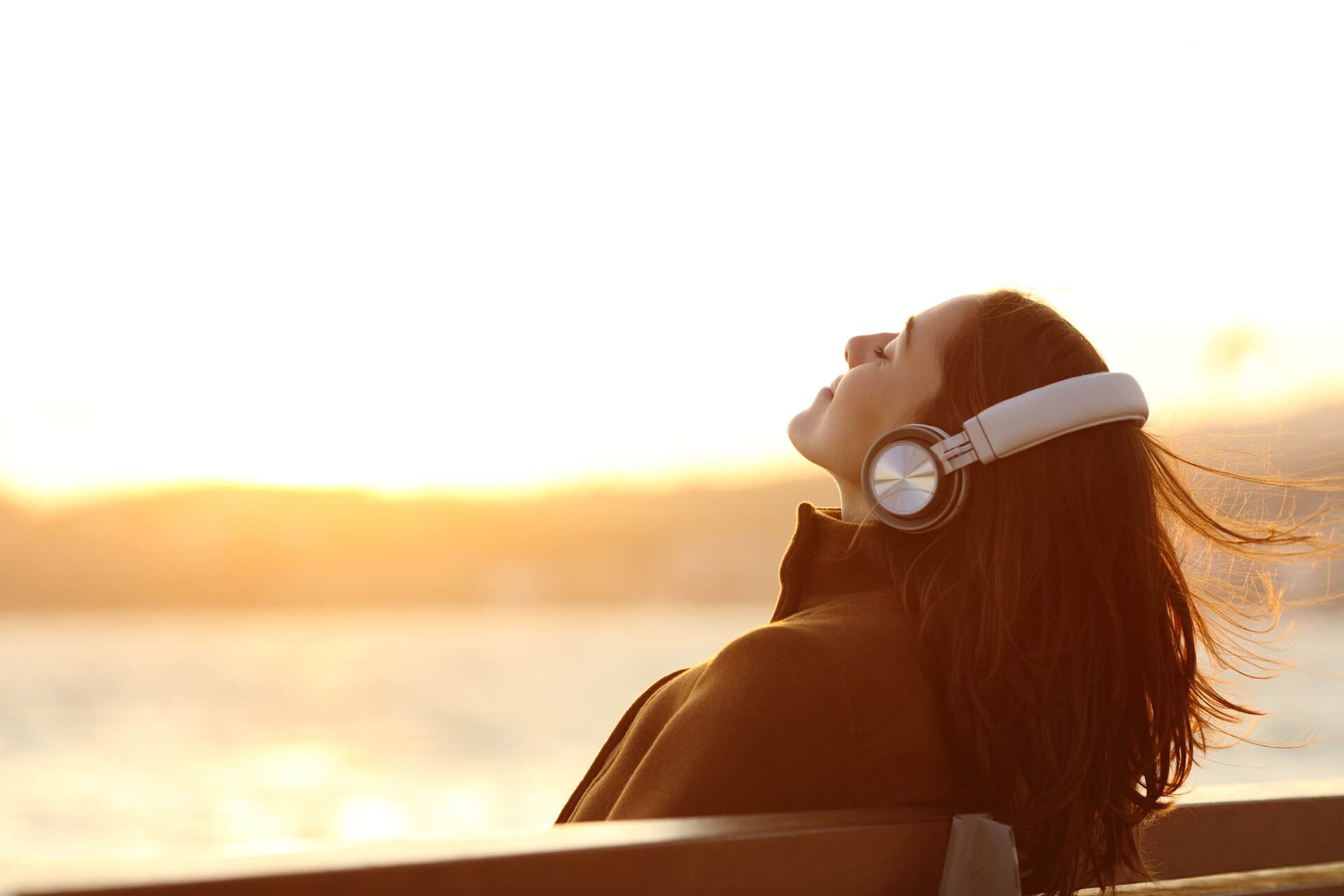 A woman is sitting on a bench wearing headphones and listening to music.