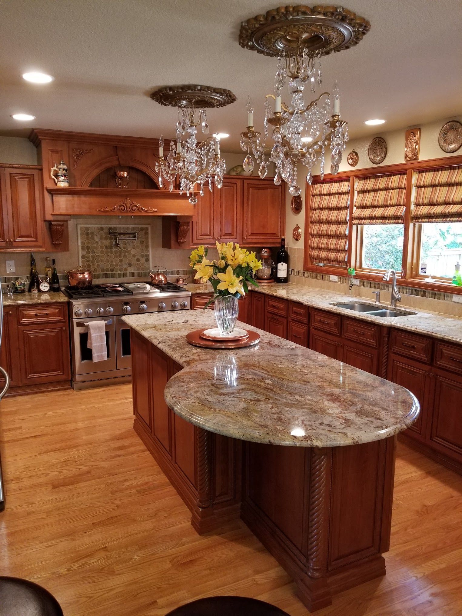 Elegant kitchen with wood cabinets, island with granite countertop, crystal chandeliers, and large windows.