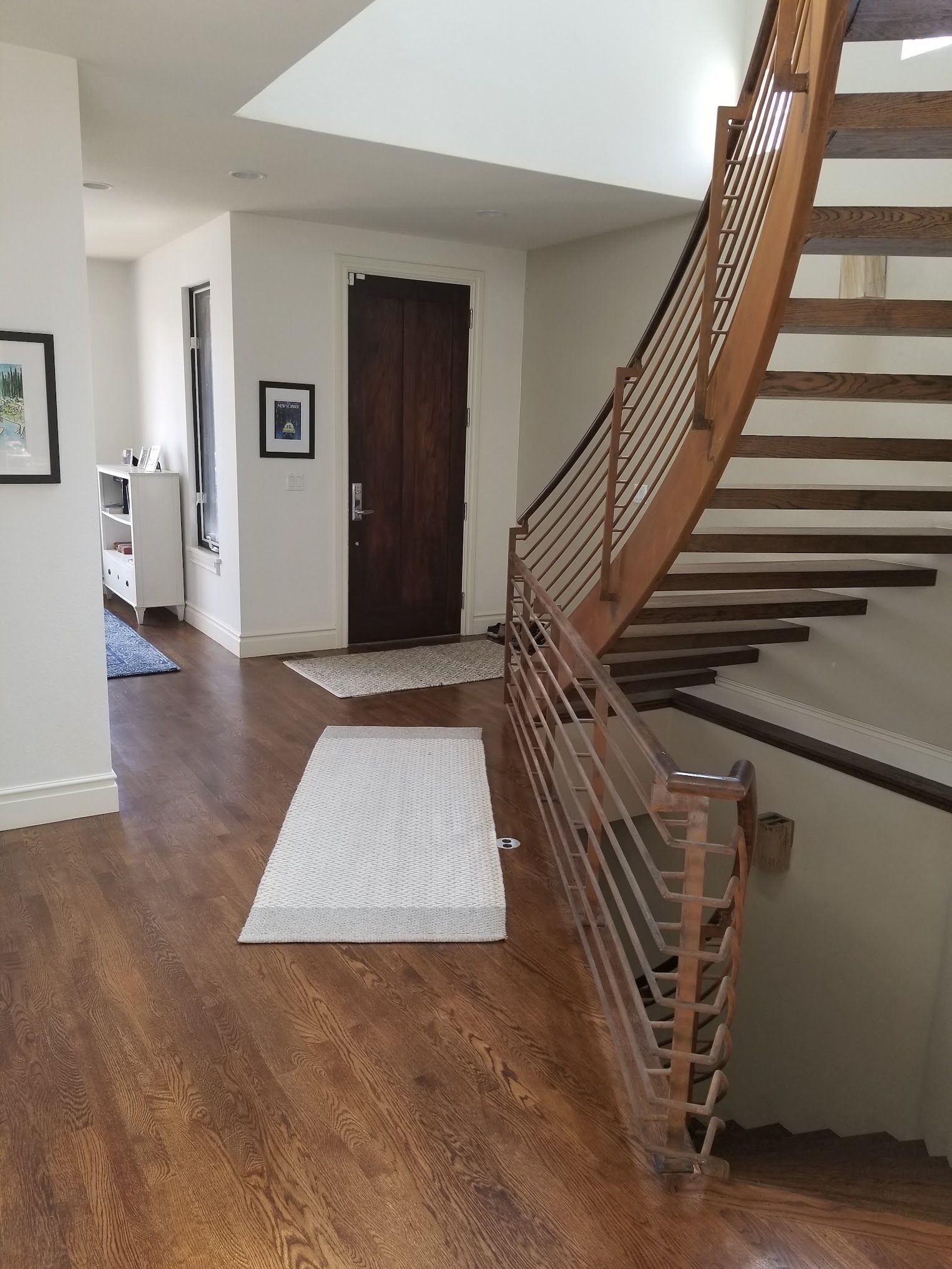 Wooden staircase with metal railing, leading to an entrance hall with a dark wooden door and hardwood floors.