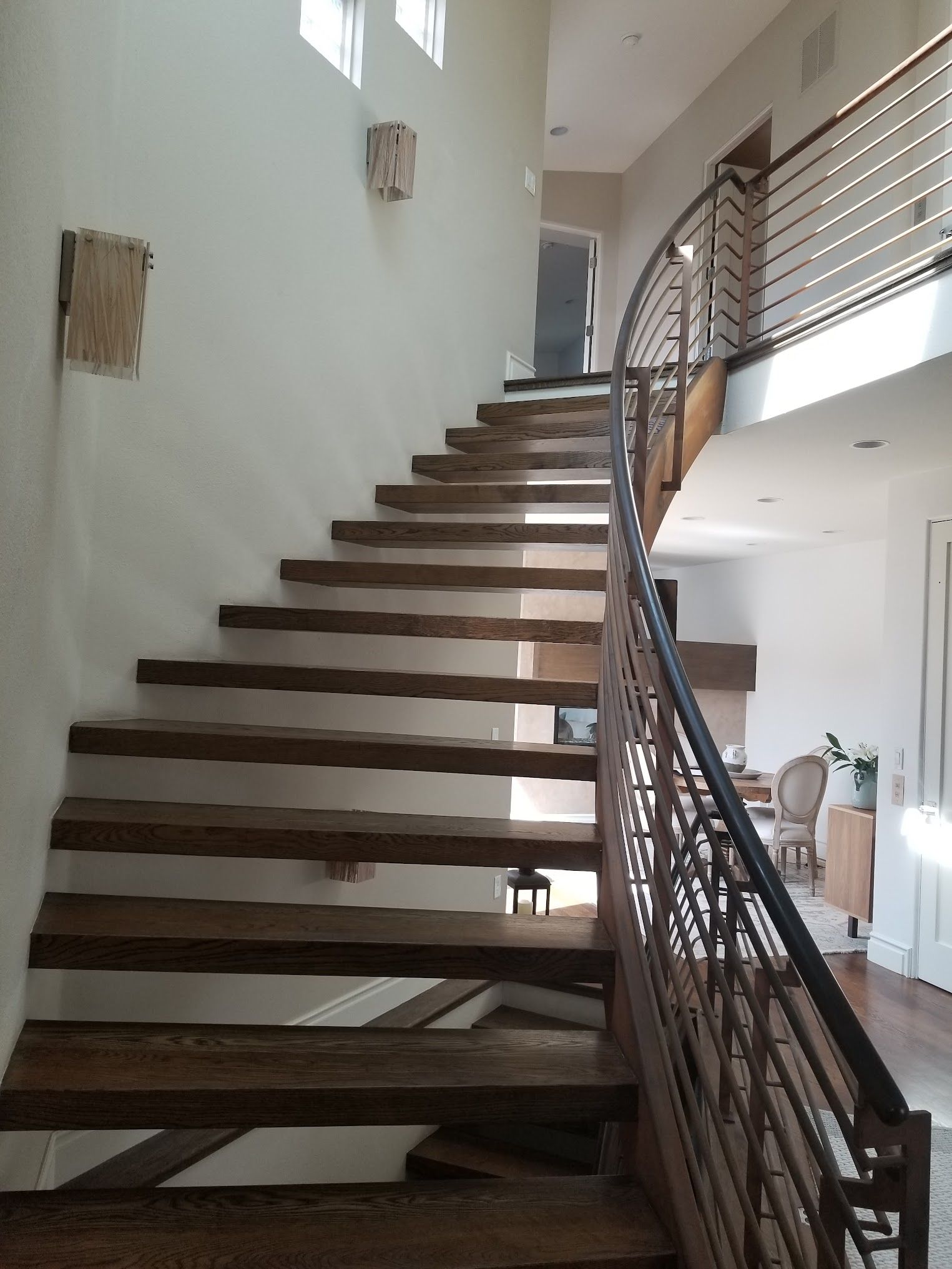 Wooden staircase with curved railing, leading to upper level.
