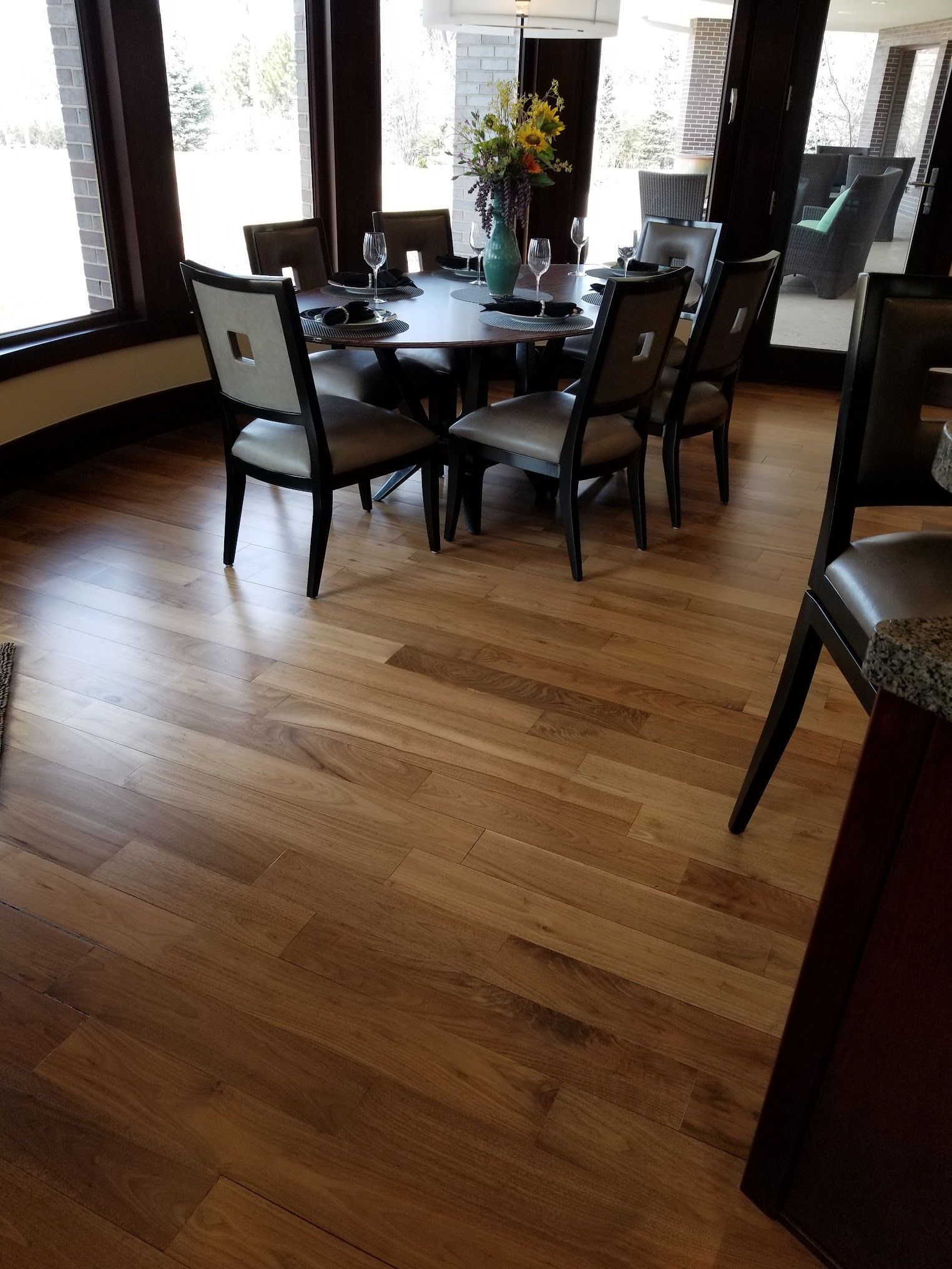 Dining room with dark wood floor, round table set for guests, and large windows.