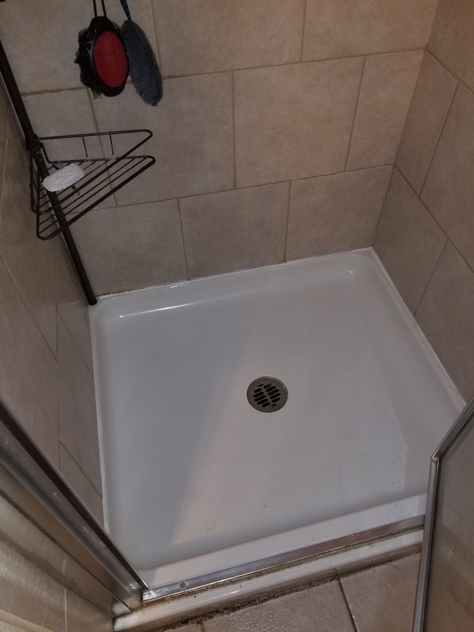 White shower base with central drain, enclosed by tiled walls, with a corner shelf.