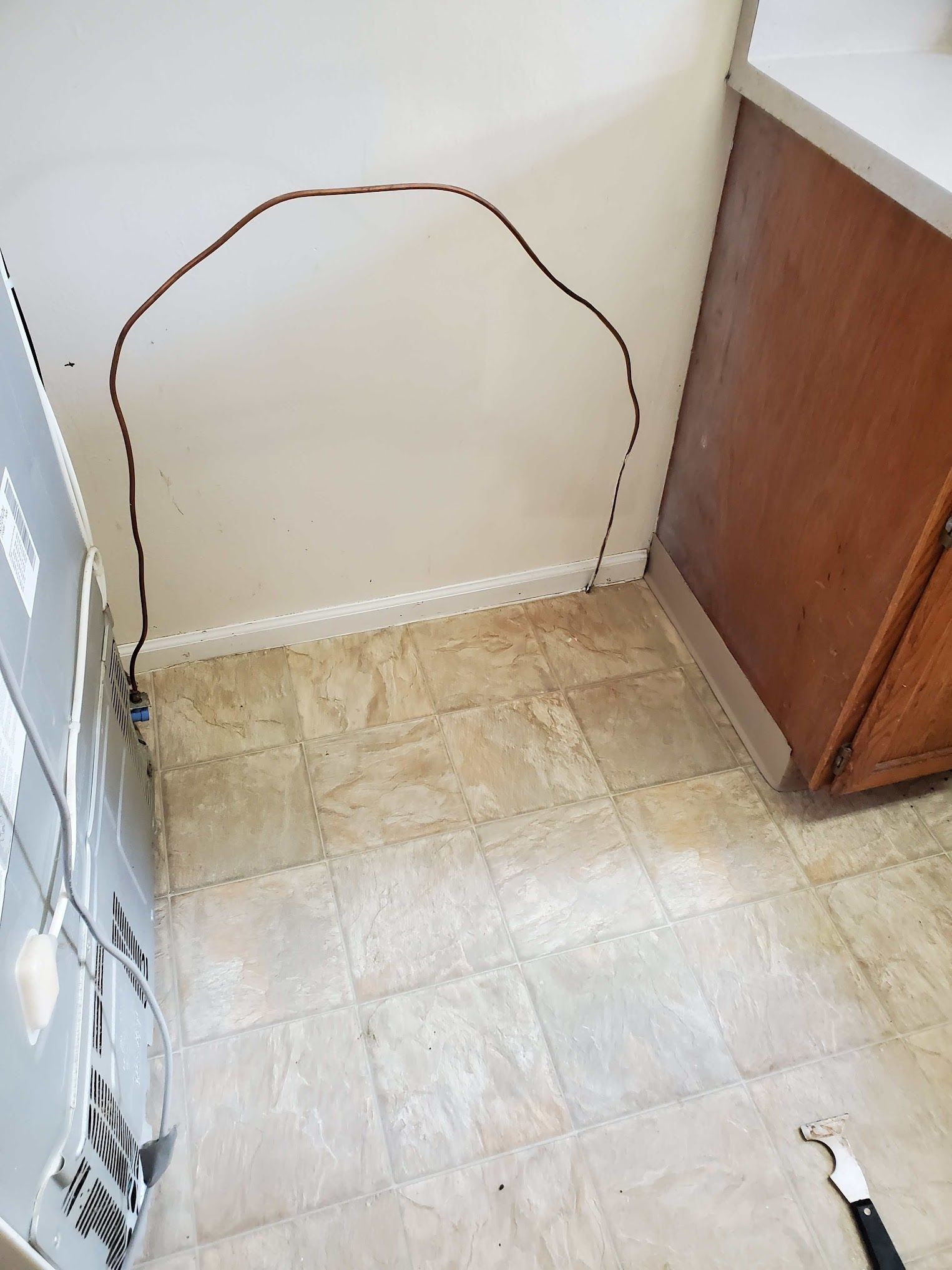 A kitchen wall with a brown outline. Beige floor and brown cabinets, a refrigerator on left.