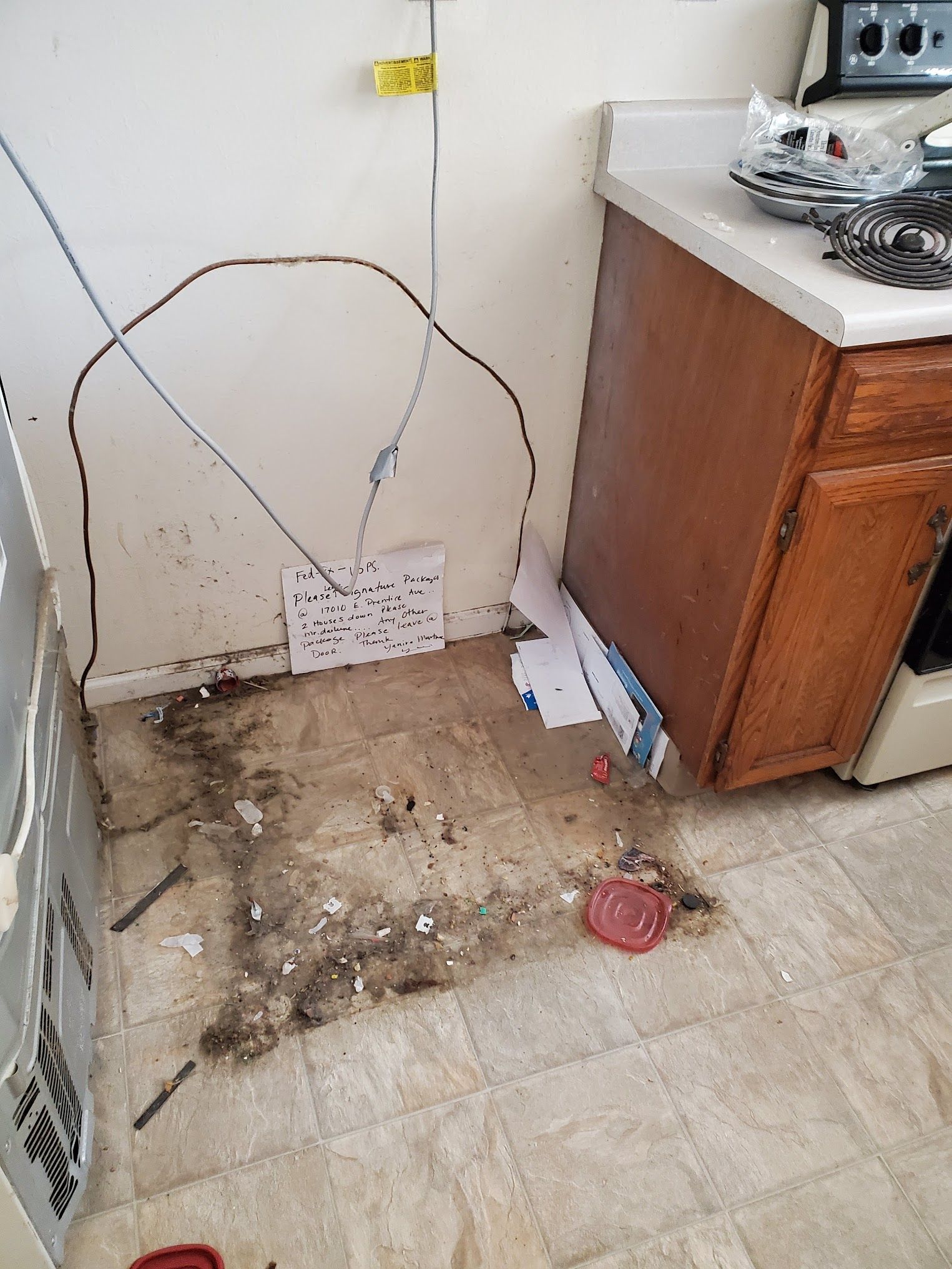Kitchen with damaged flooring, exposed wall, wires, and a cabinet.