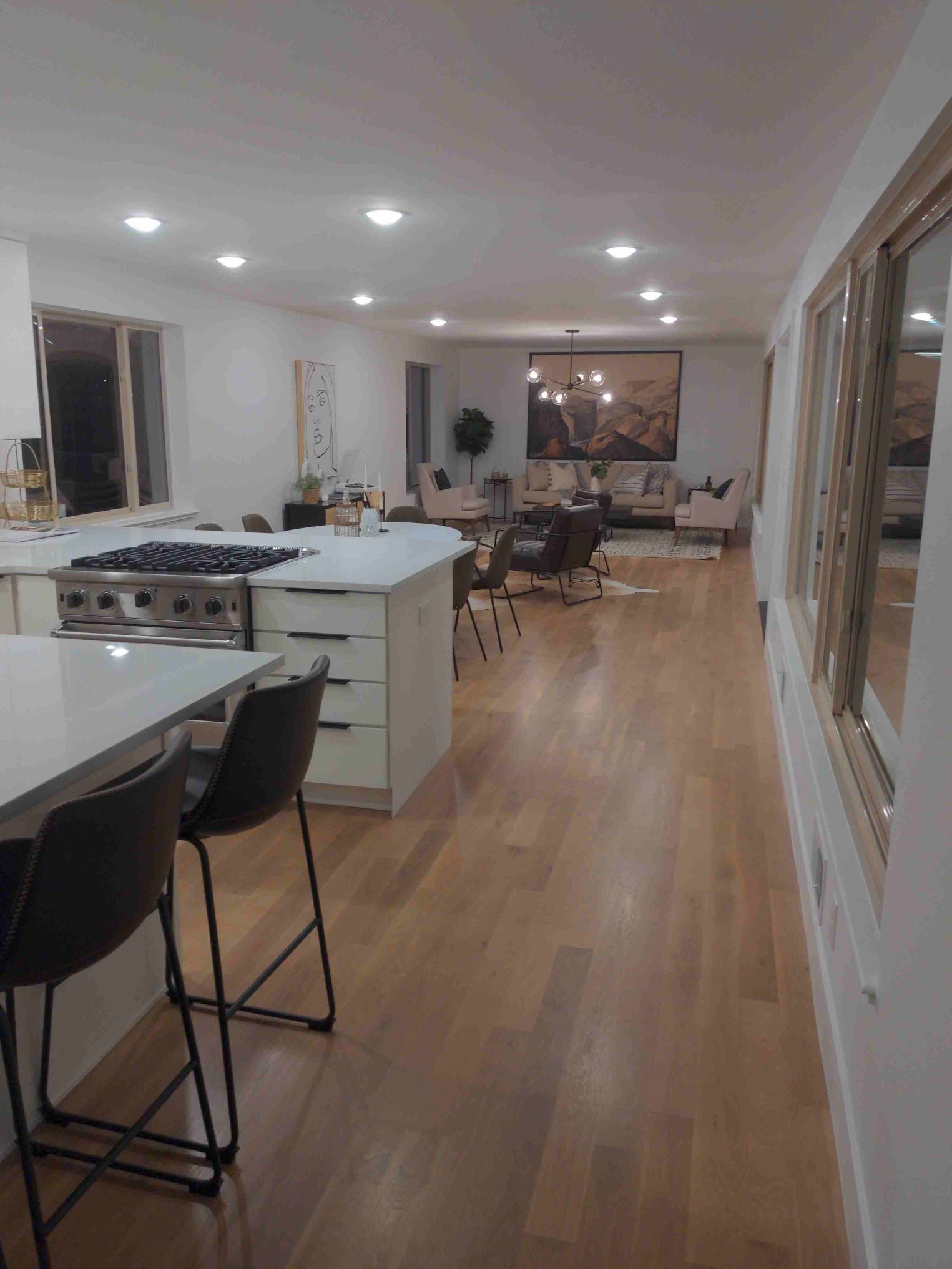 Modern kitchen and living area with hardwood floors, island with bar stools, and recessed lighting.