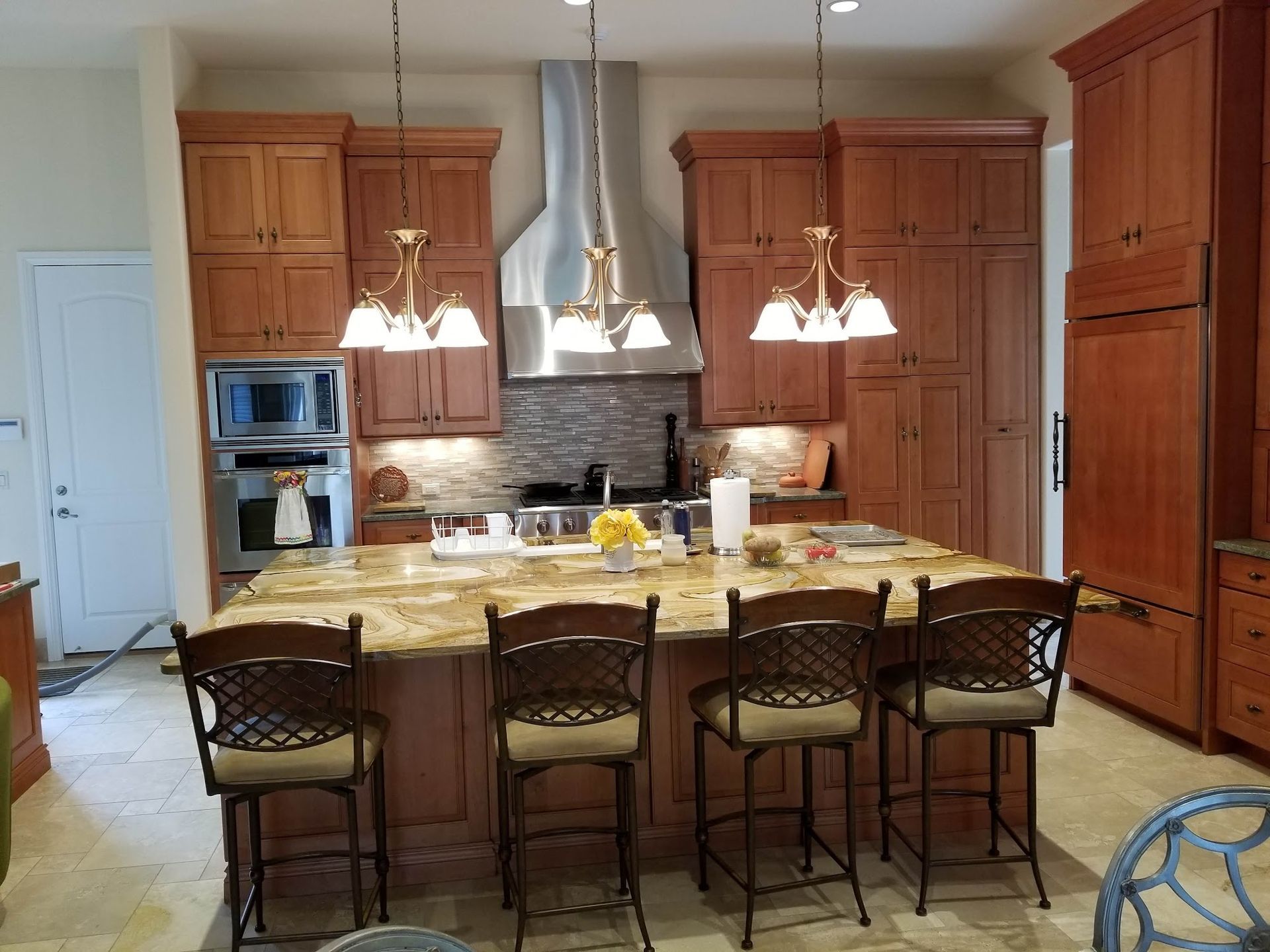 Kitchen with island, cabinets, and bar stools. Brown cabinetry, granite countertops, and four bar stools.