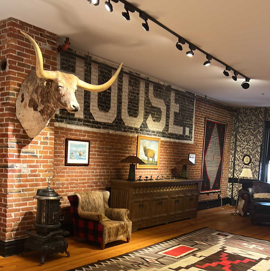 Room with brick walls, a longhorn head, antique furniture, and a large “HOUSE” sign.
