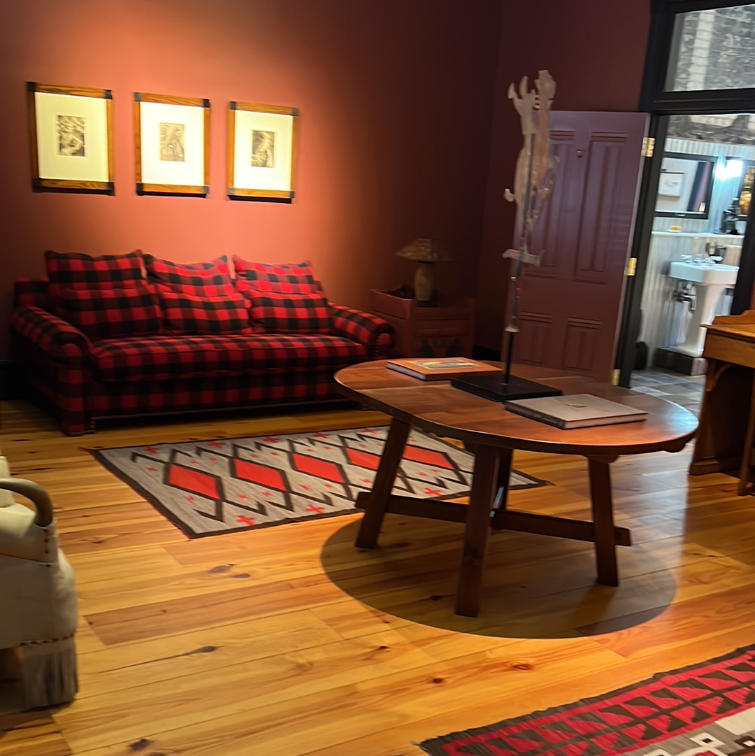 A cozy living room with plaid sofa, wooden table, and colorful rug. Red walls and wood floors.