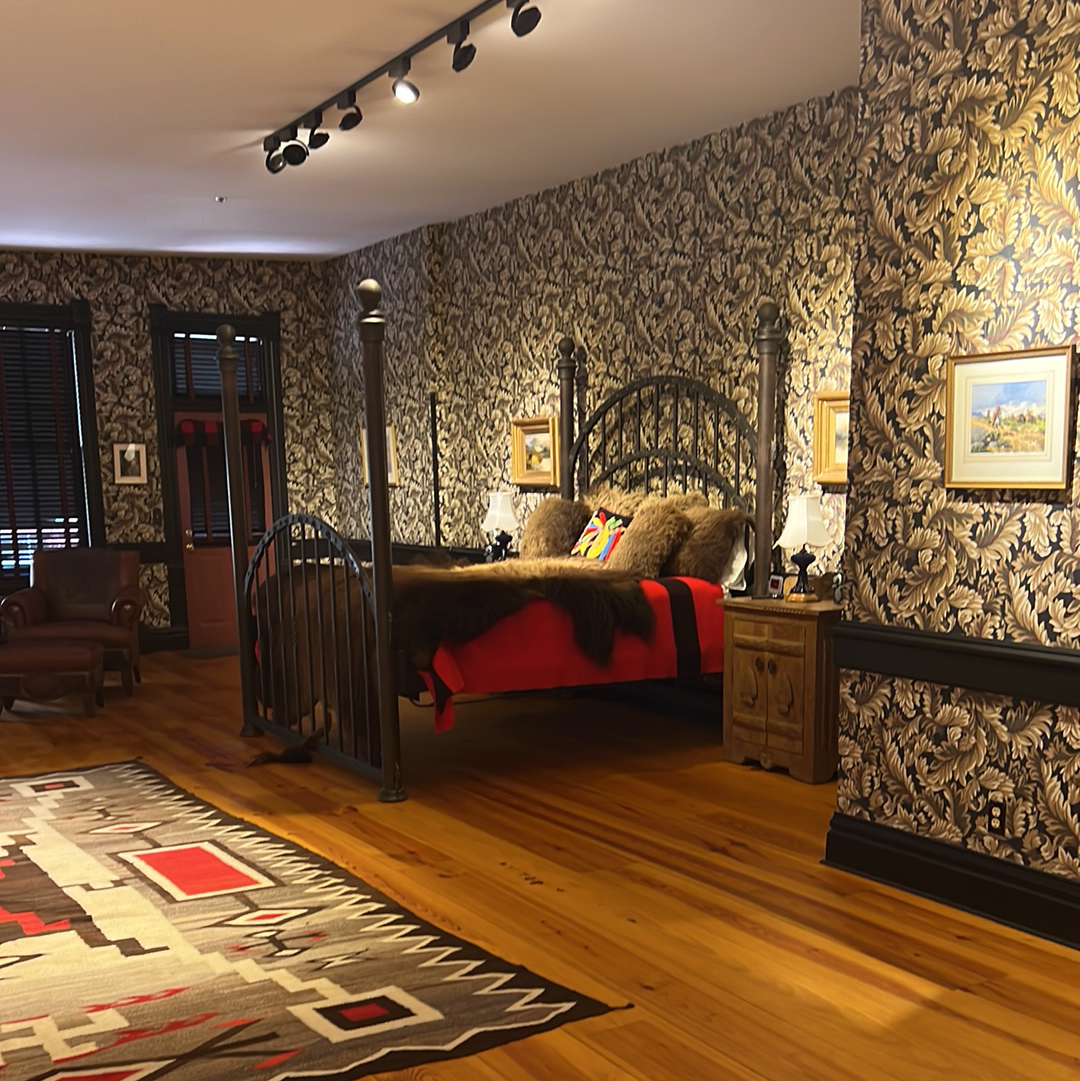 Bedroom with patterned wallpaper, dark bed frame, wooden floor, and area rug.