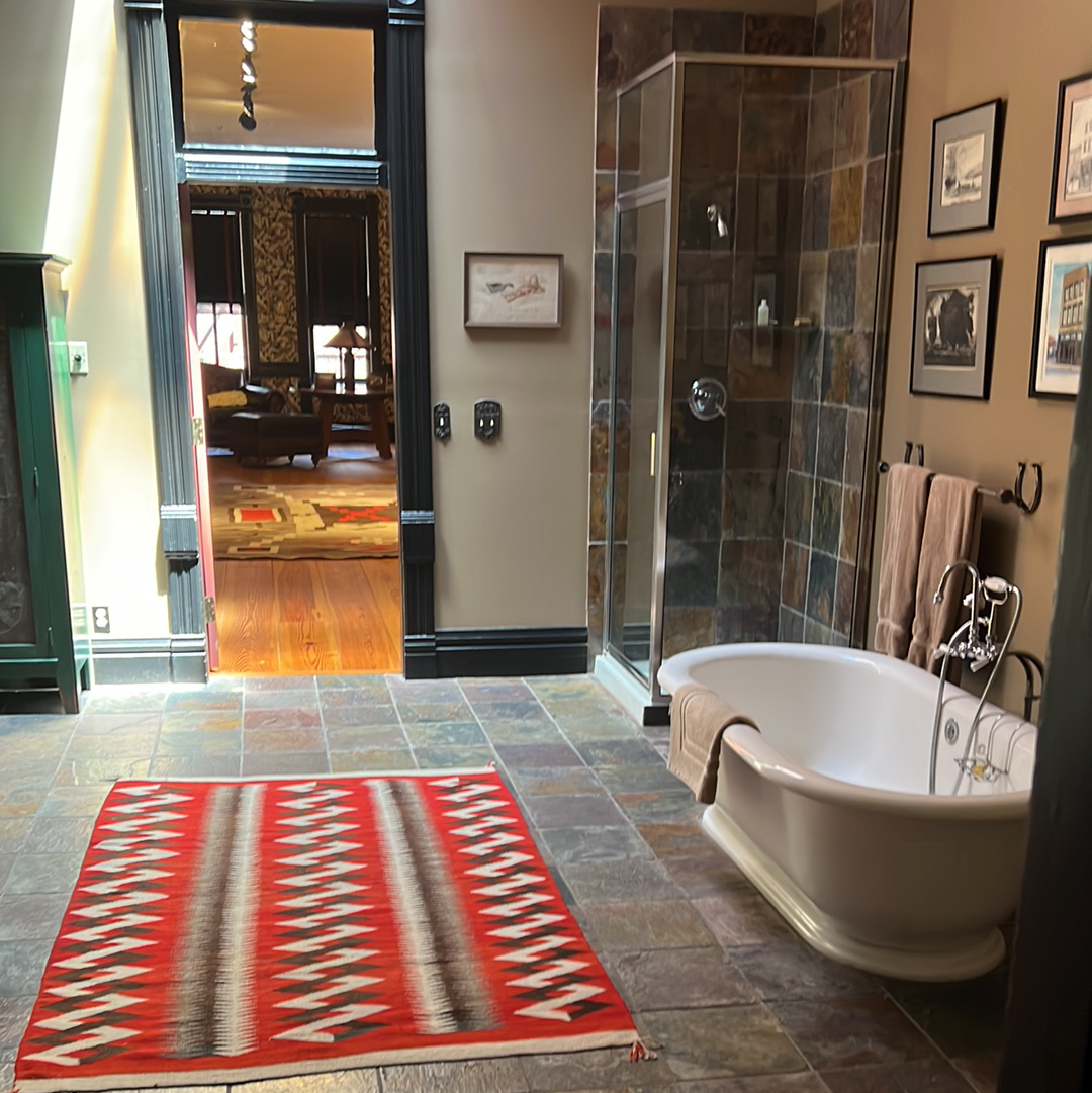 Bathroom with a red rug, white tub, glass shower, and framed art.