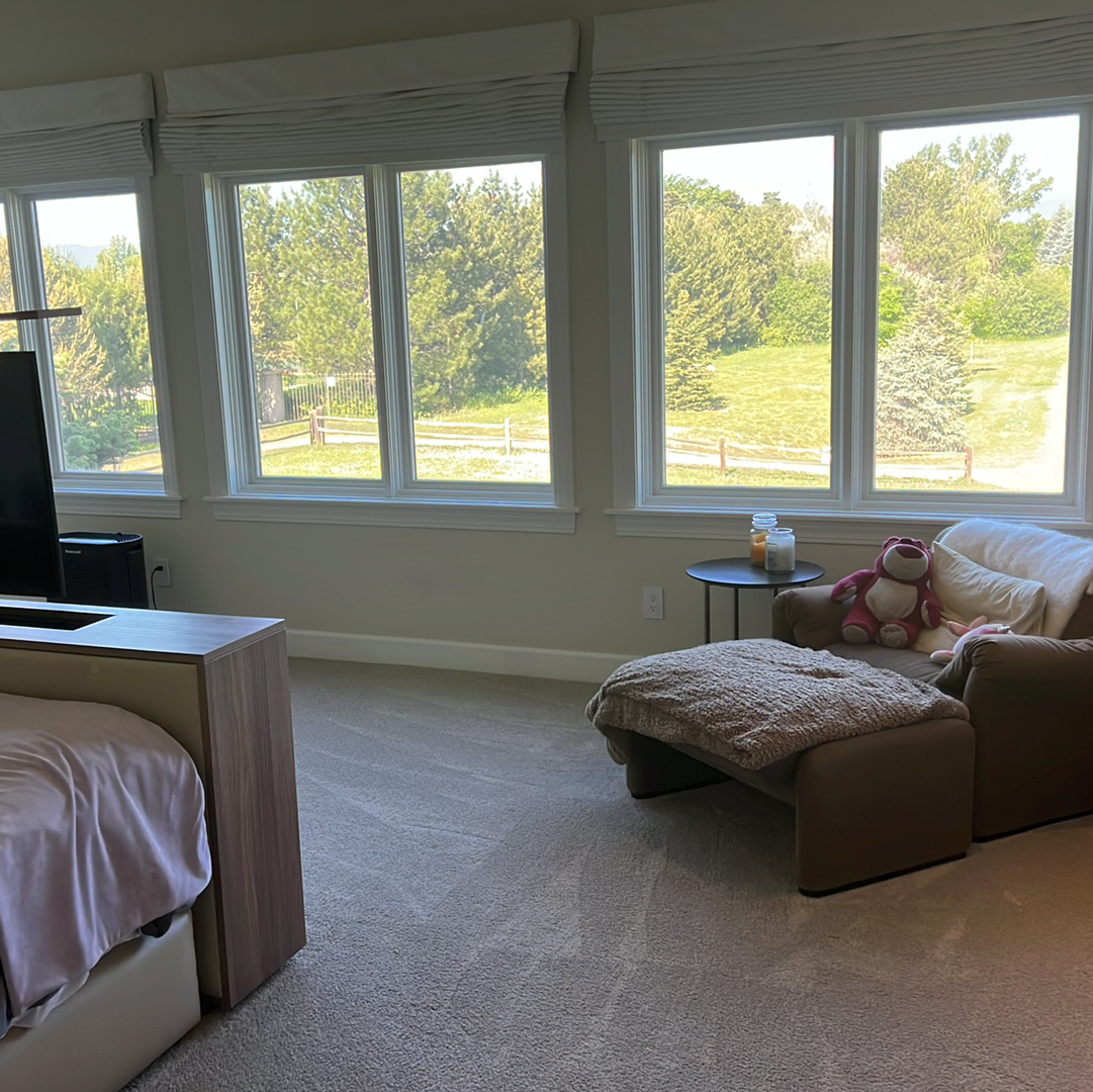 A bright room with a large window, a chaise lounge, and a bed.