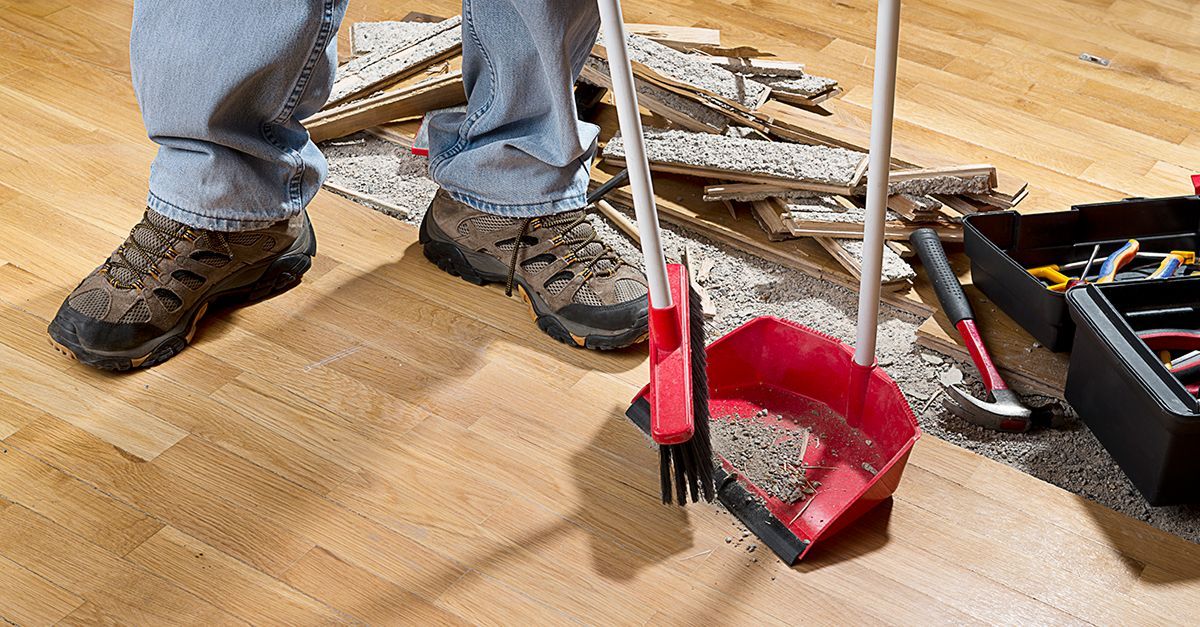 Shovel and broom next to three bags of material on a concrete floor.