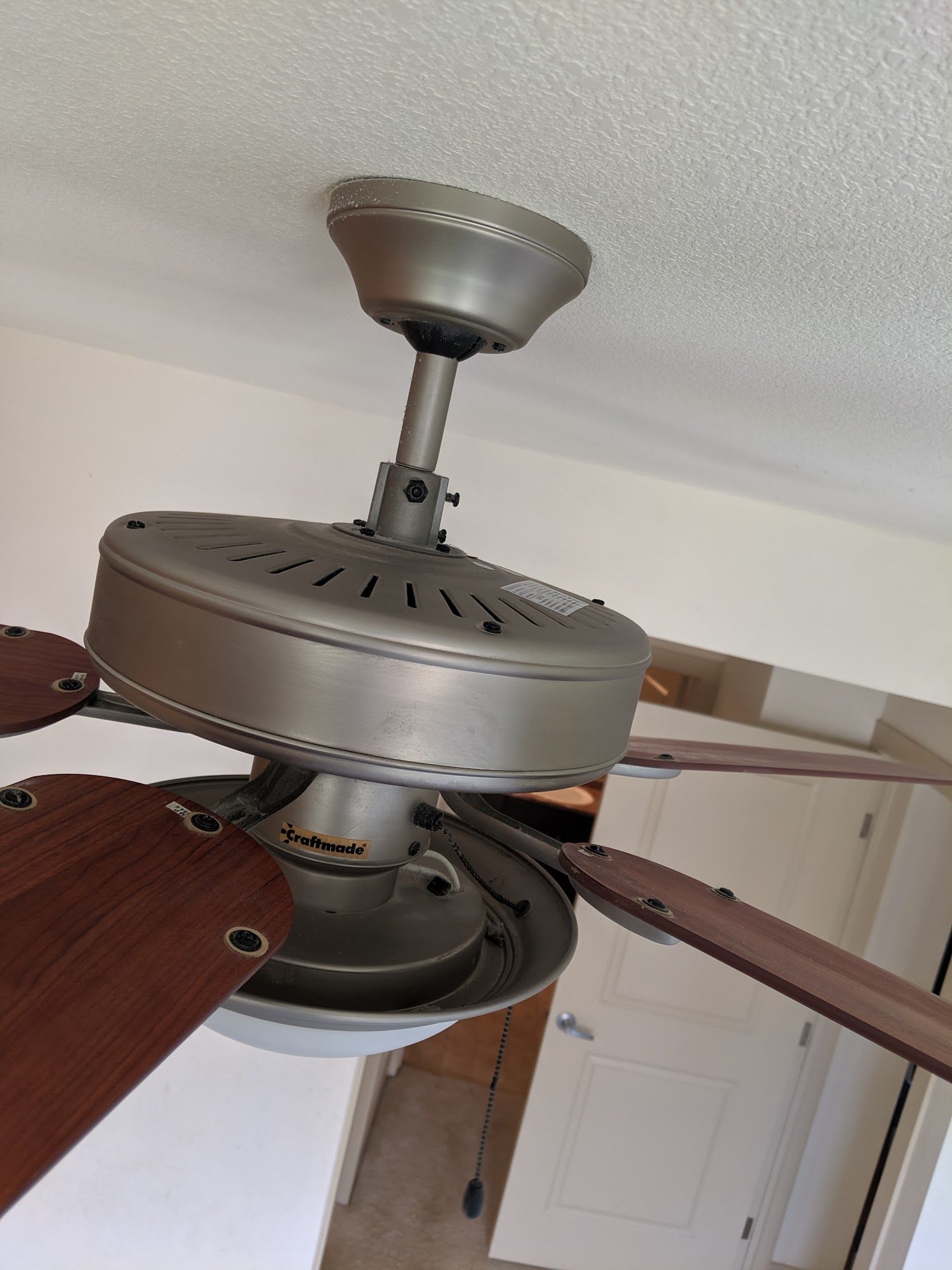 Ceiling fan with dark wood blades and a brushed metal finish, hanging from a white ceiling.