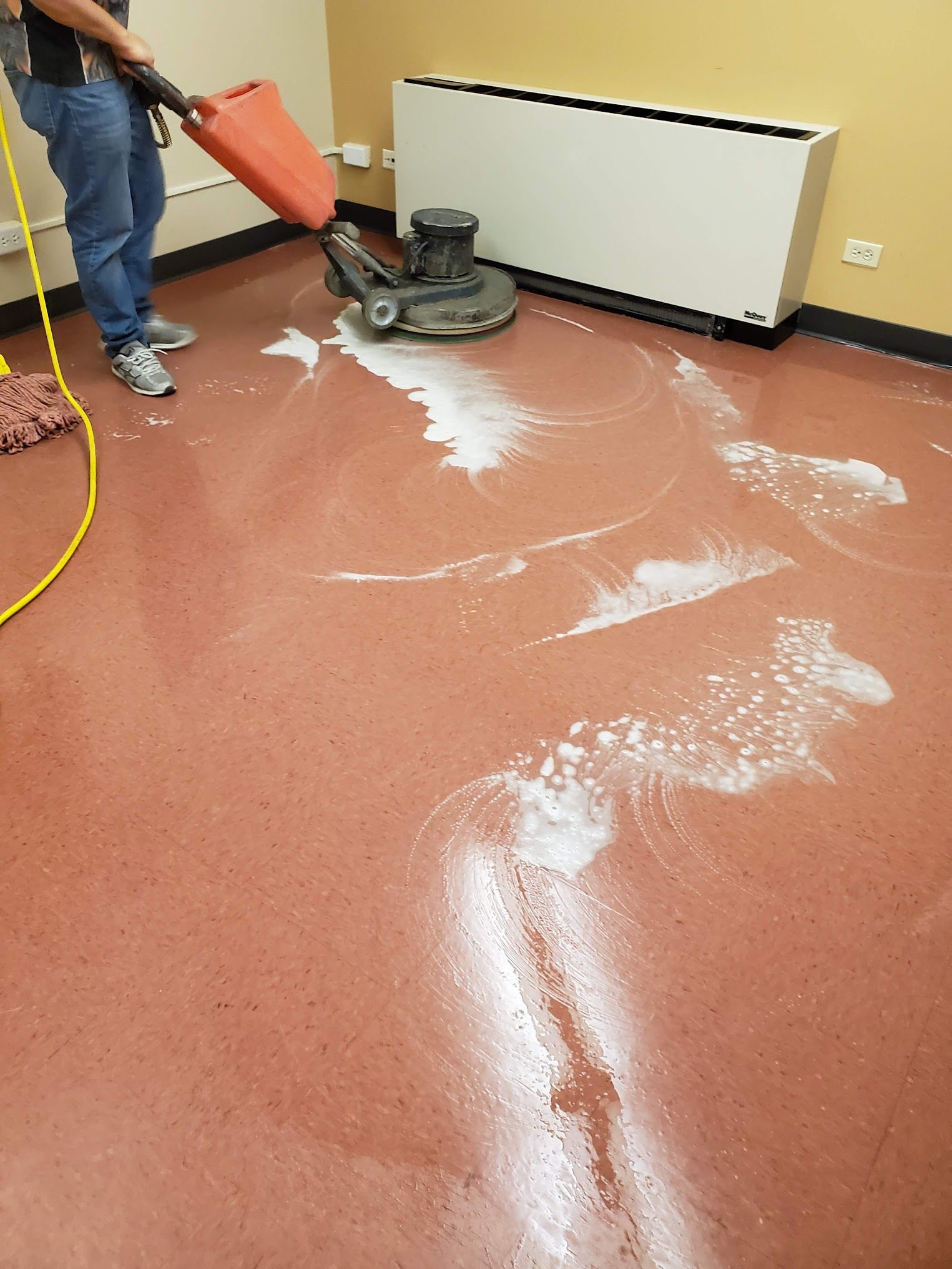 Person using a floor buffer with white suds on a red floor.