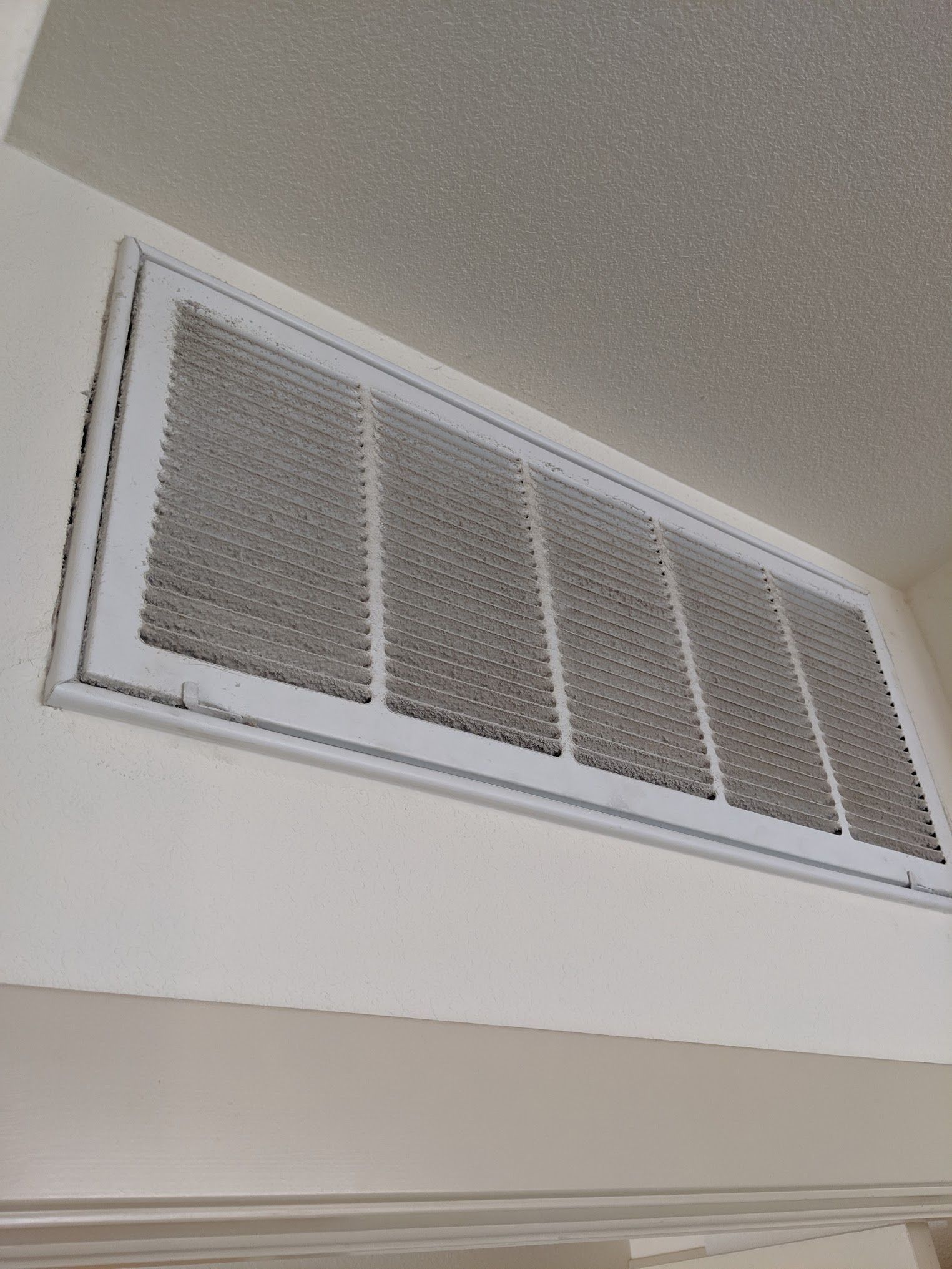 White air vent in a white ceiling. The vent has a metallic grill and is rectangular.