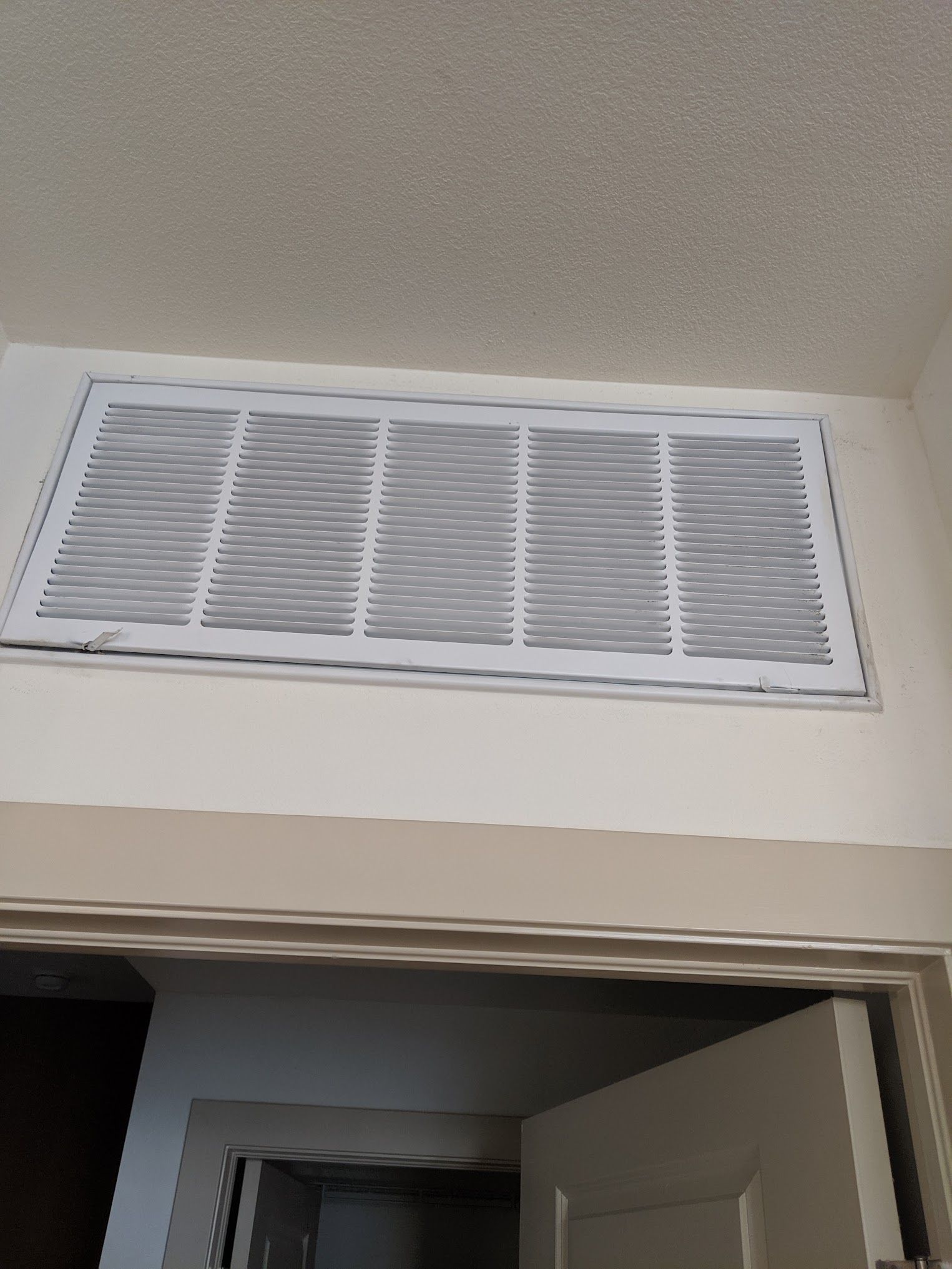 White air vent in a white ceiling, above a doorway with a closed white door.
