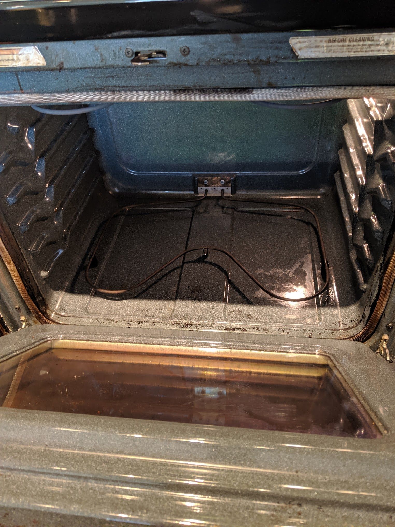Inside of an oven with the door open; the interior is dark and shows the heating element and some grime.