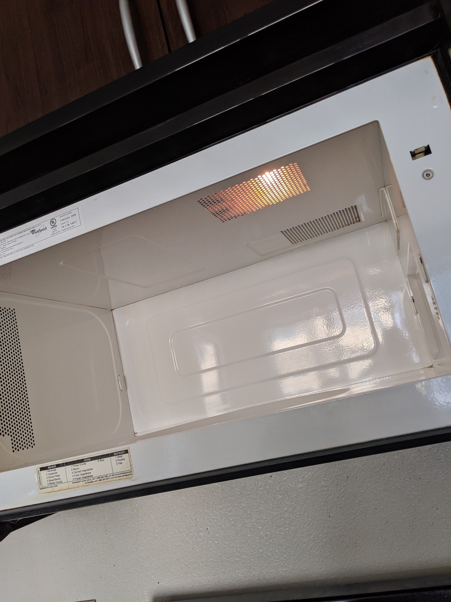 Empty, open microwave with a lit interior light. The inside is white, with a white rectangular piece at the bottom.