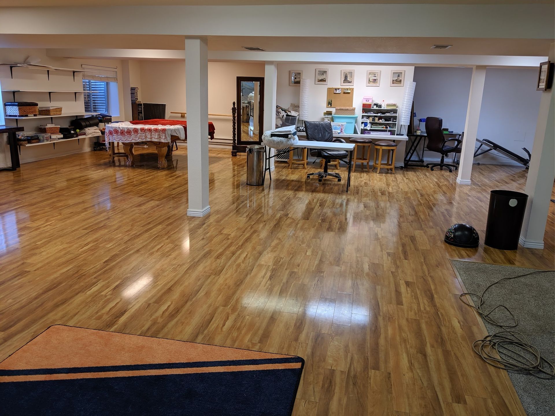 Large room with wood floors. Several tables and work areas. Brightly lit with white walls and columns.