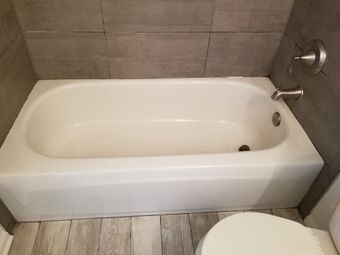 White bathtub built into gray tiled wall, next to toilet.