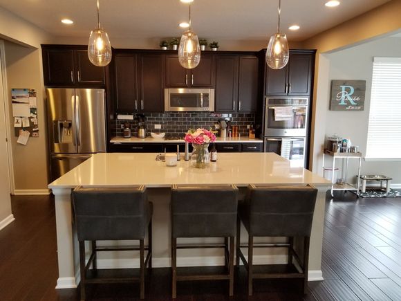Modern kitchen with dark cabinets, white island, stainless steel appliances, and three bar stools.