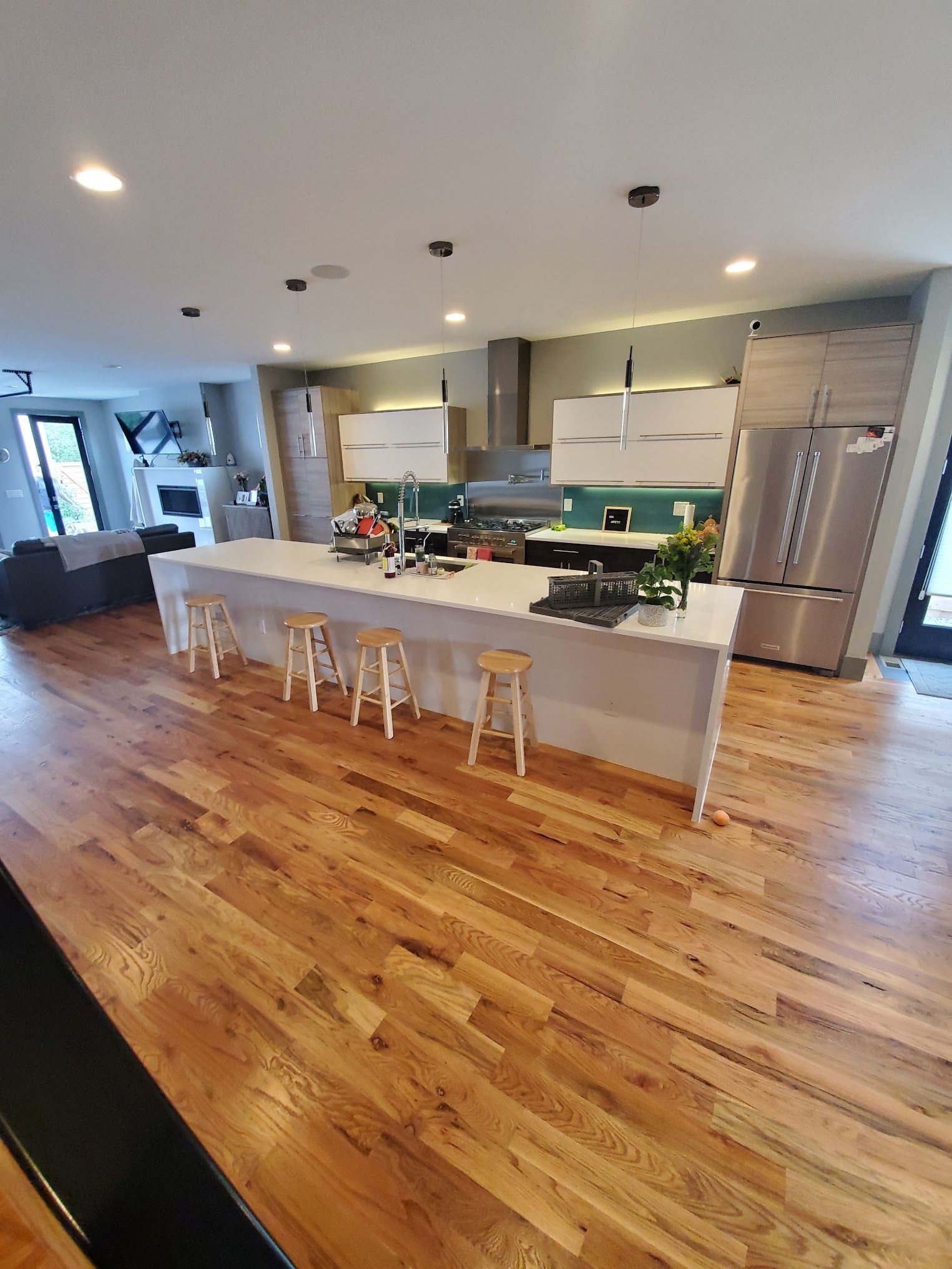 Modern kitchen with large island, light wood floors, white cabinets, and stainless steel appliances.