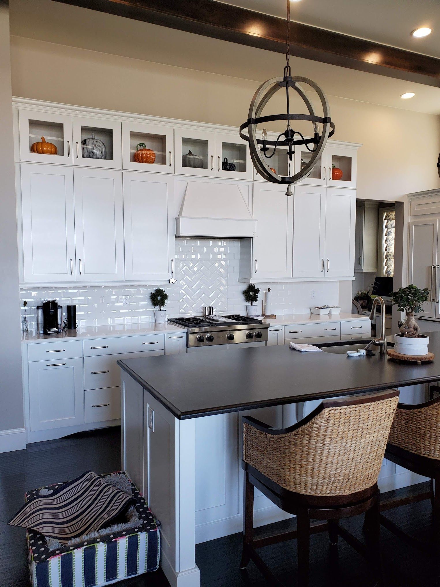 White kitchen with dark island, decorative overhead light, wicker bar stools.