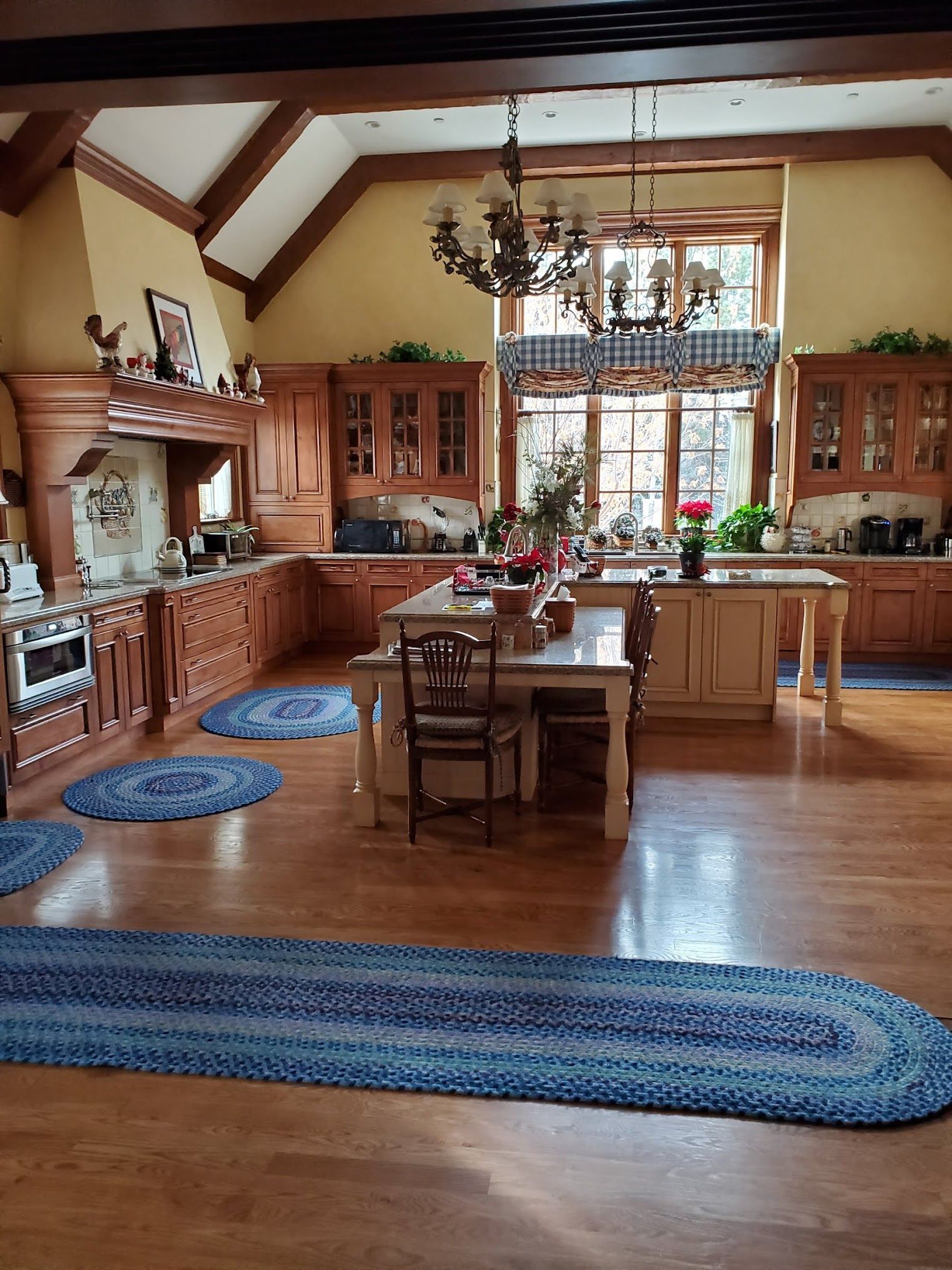 Spacious kitchen with wood cabinetry, two islands, and blue braided rugs on hardwood floors.