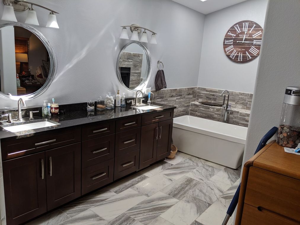 A bathroom with dark brown cabinets, two round mirrors, and a large clock on the wall.