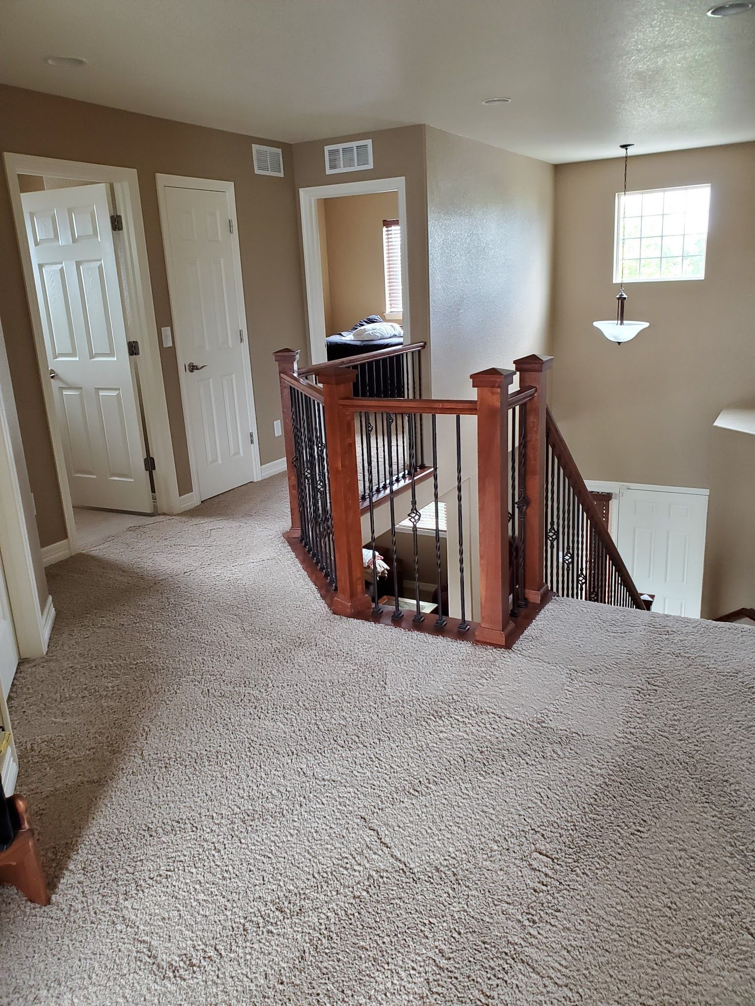 Carpeted upstairs hallway with stairs, doors, and decorative railing.