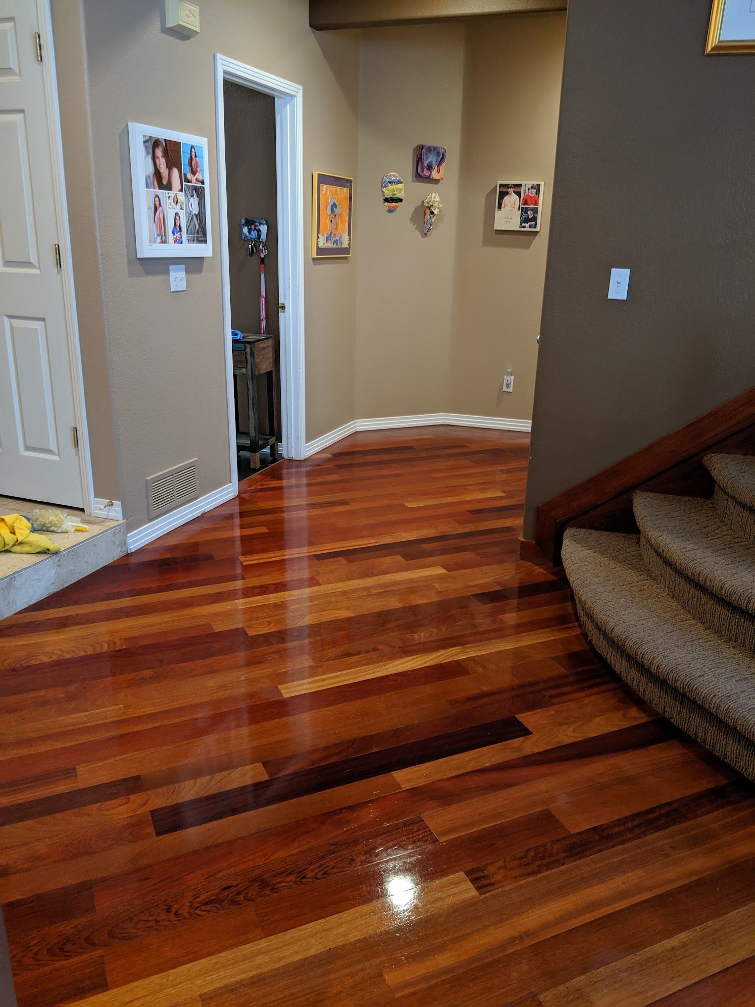 Hallway with glossy, multi-toned wood floors, tan walls, and a staircase.