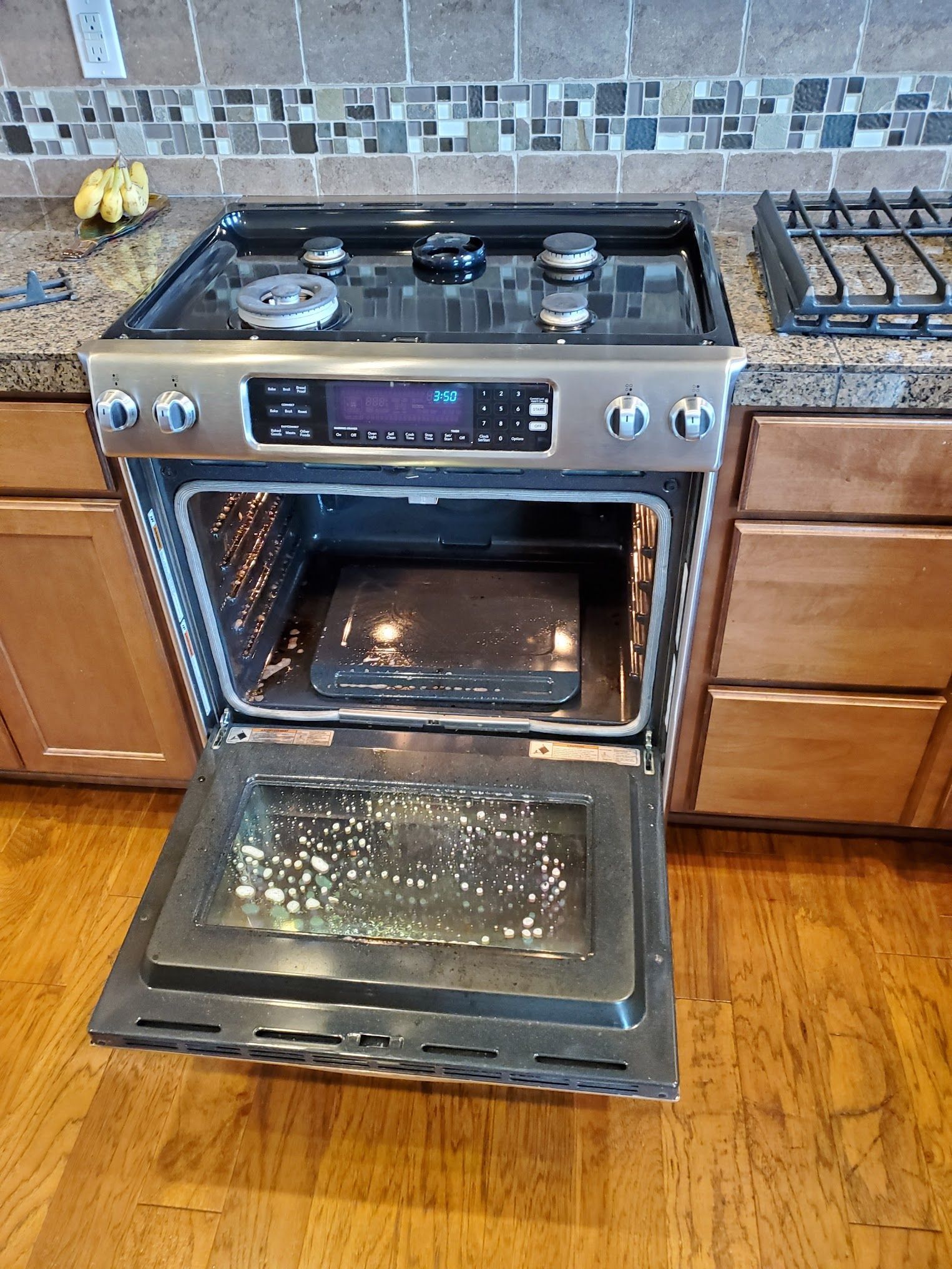 A stainless steel oven with the door open, showing a dirty interior and a baking tray.