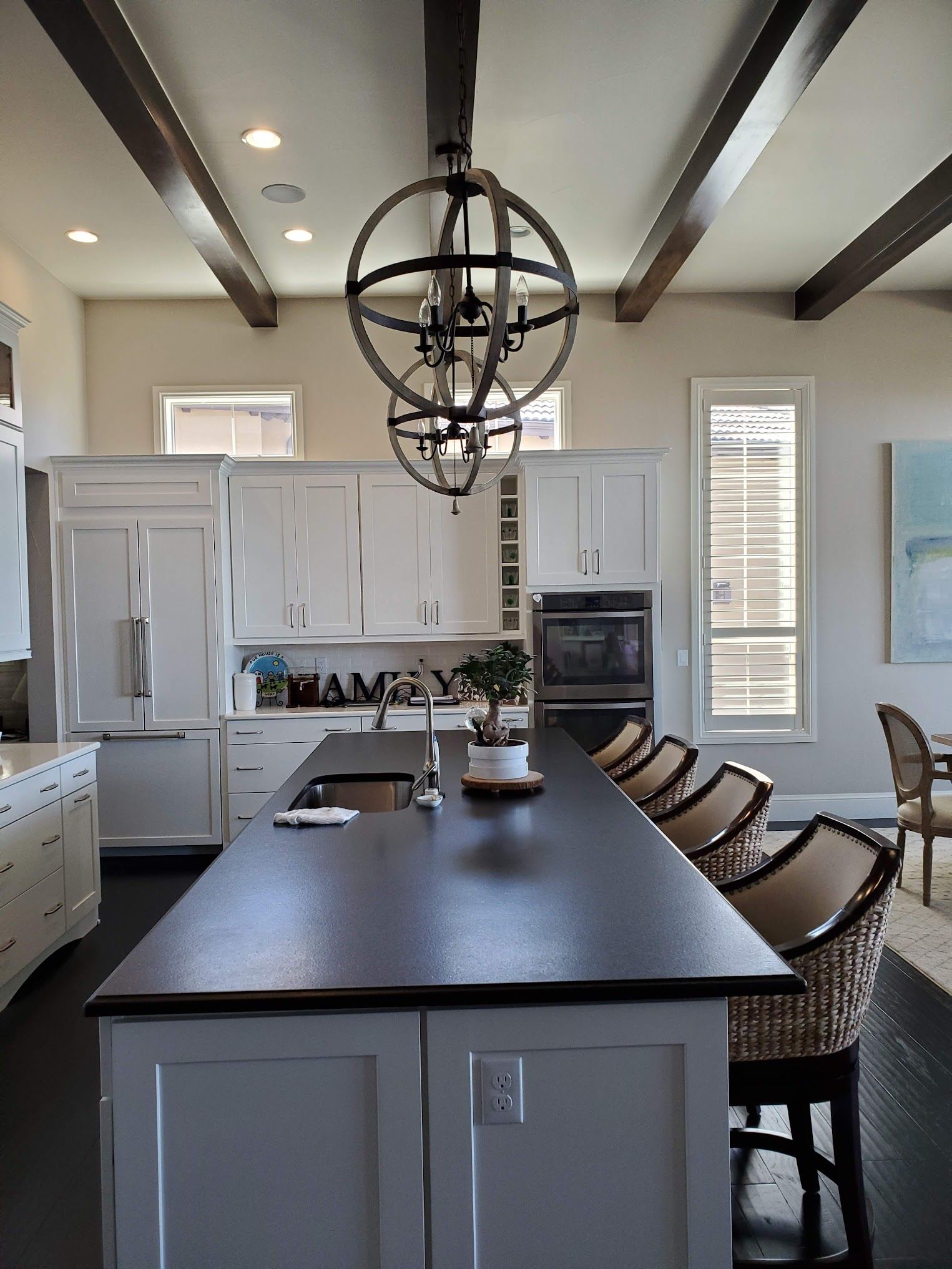 Kitchen with white cabinets, dark countertop island, globe pendant lights, and dark ceiling beams.