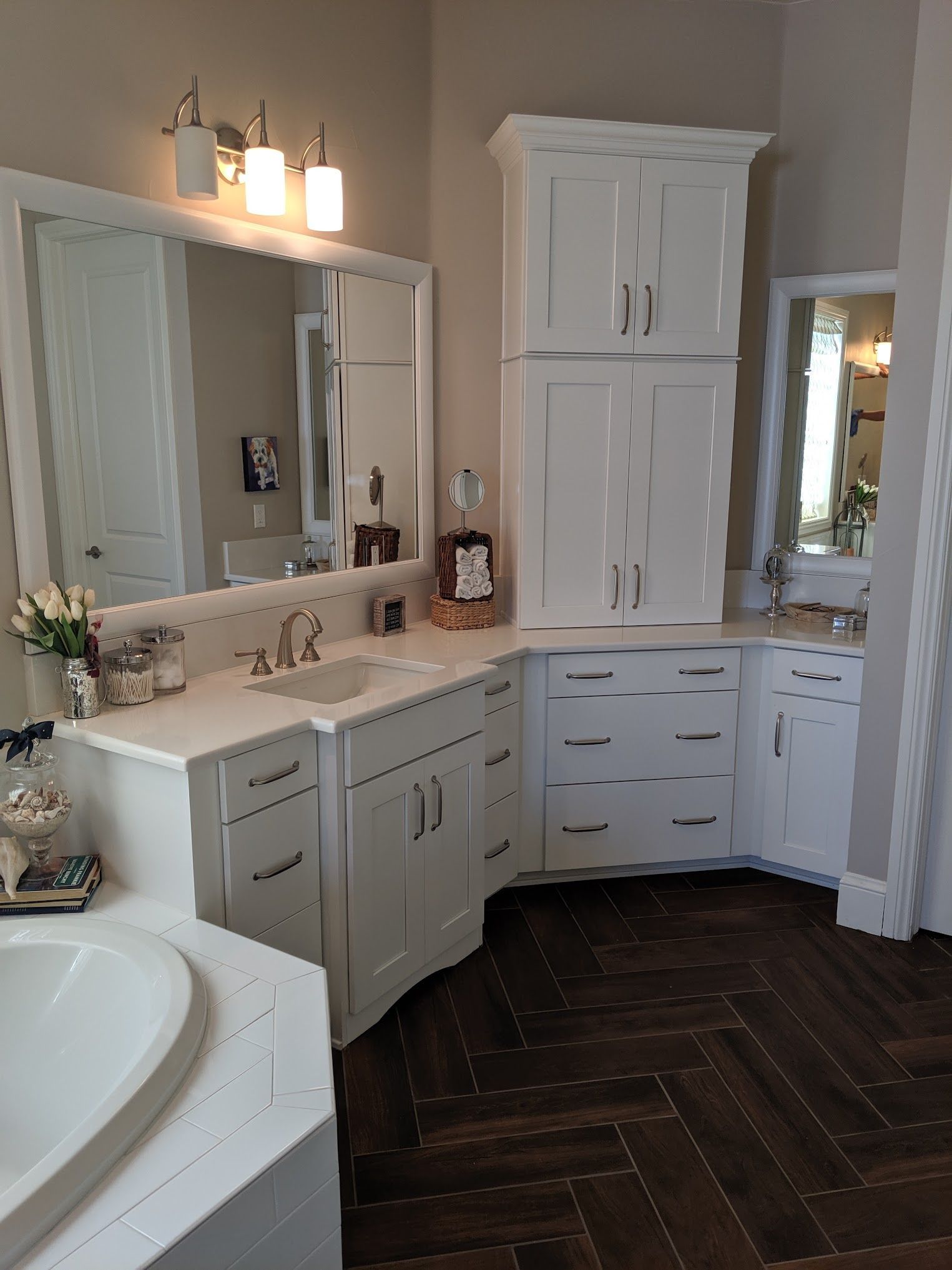 White bathroom with curved cabinets, sink, and large mirrors. Brown herringbone floor.