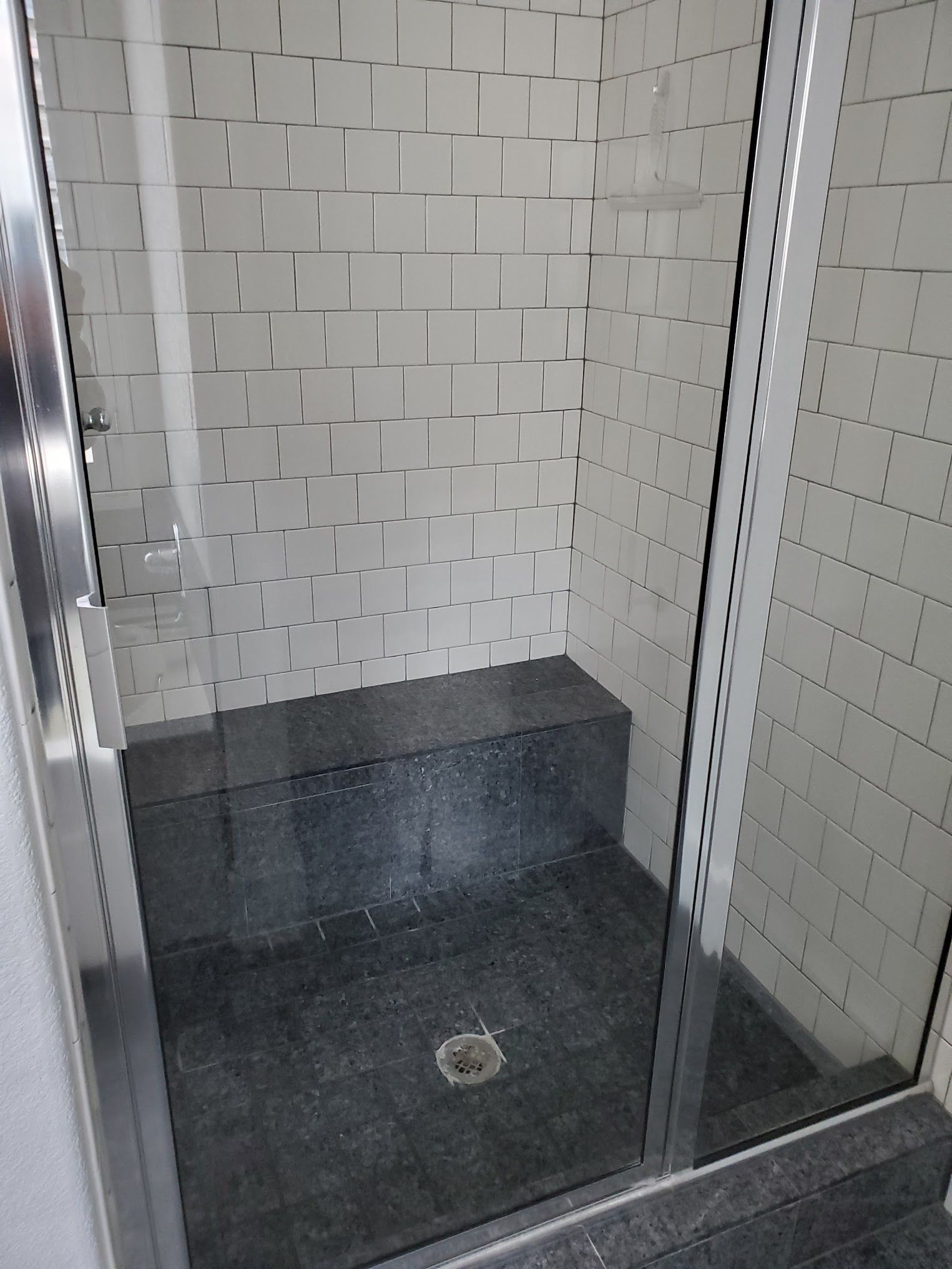 Shower stall with gray tile, a built-in seat, and glass door.