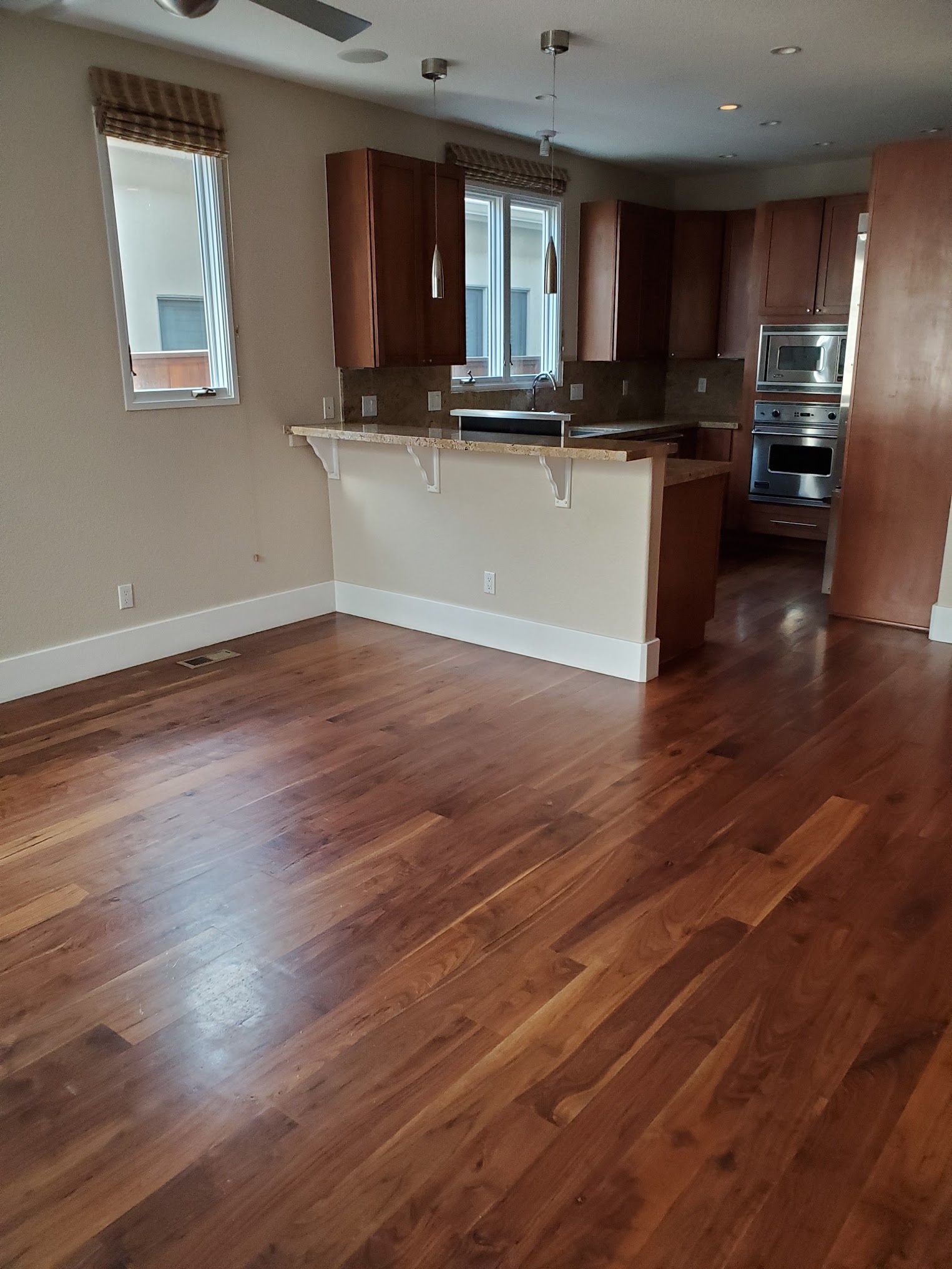 Hardwood floor leads to a kitchen with wooden cabinets, a breakfast bar, and built-in appliances.