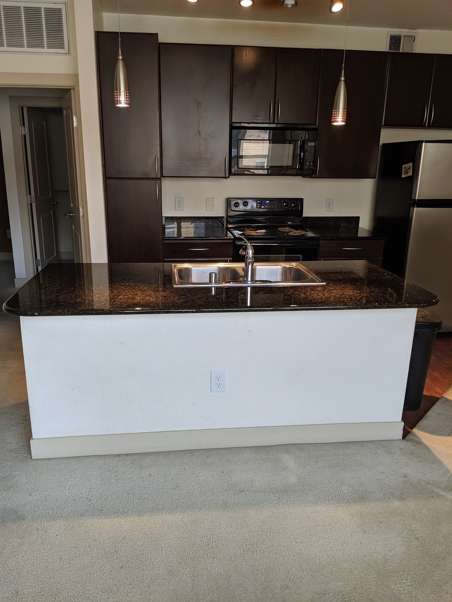 Dark brown kitchen cabinets with a black countertop island, sink, and stove.