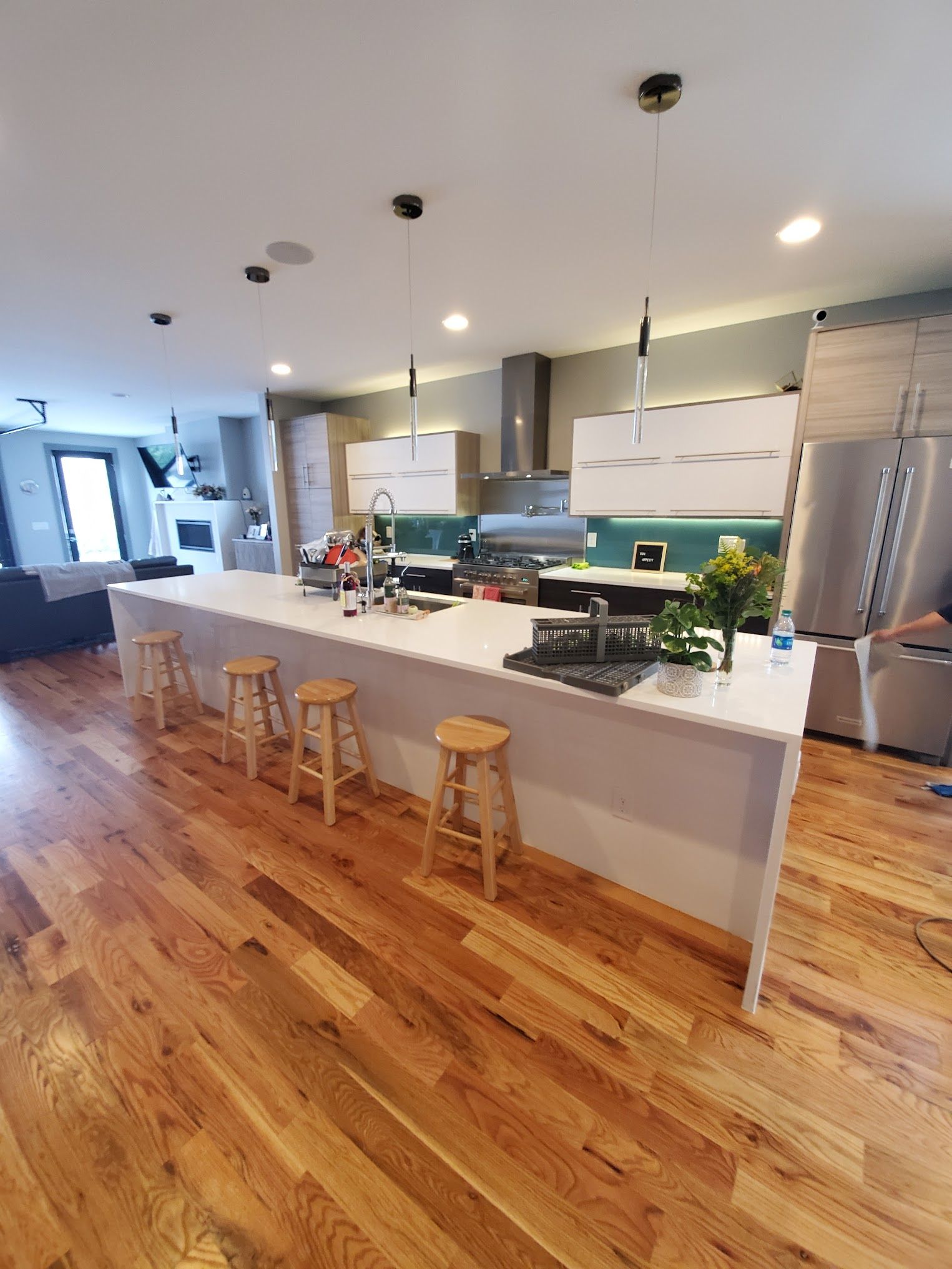 Modern kitchen with large island, wood floors, stainless steel appliances, and teal backsplash.