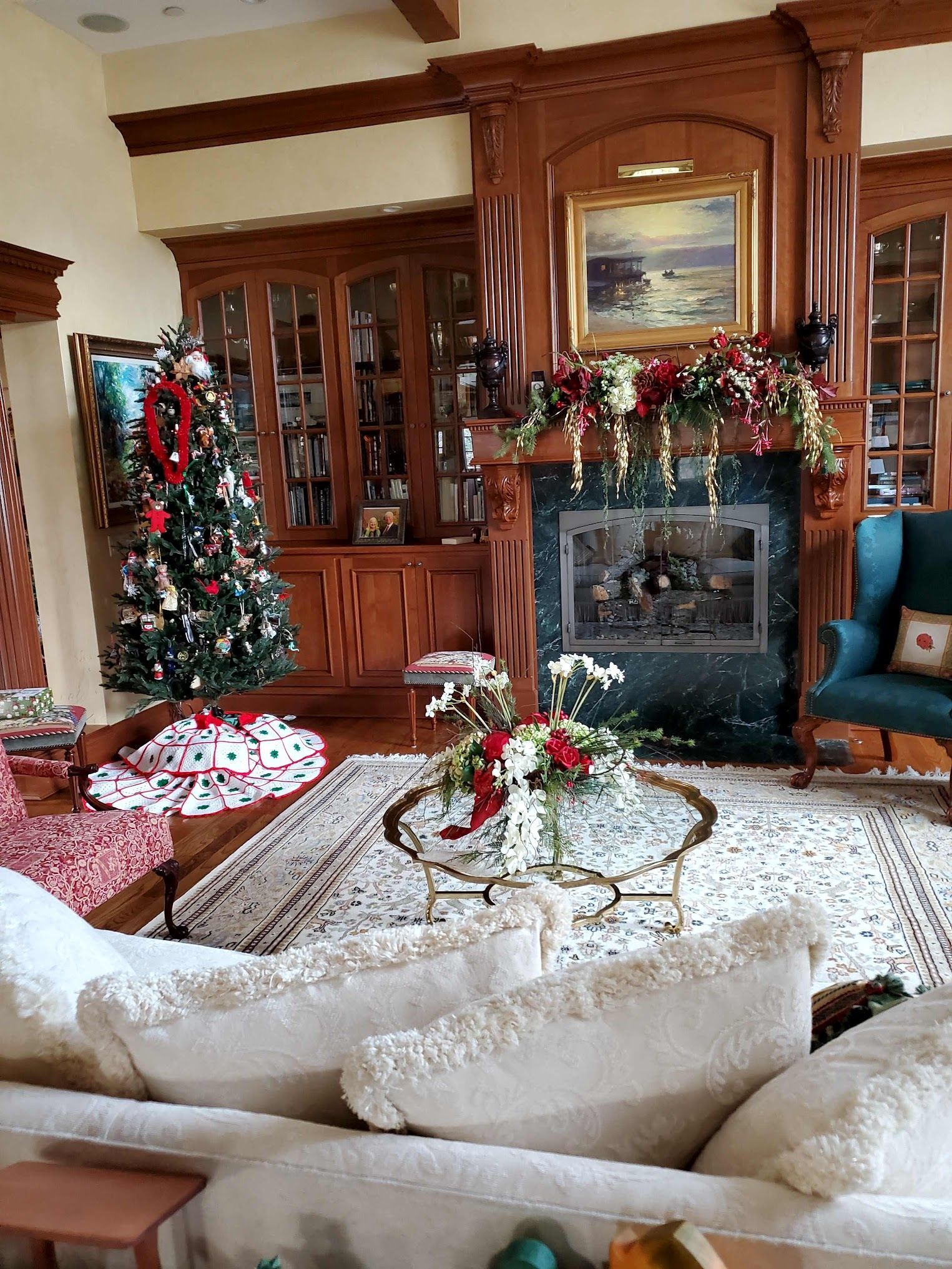 Living room with Christmas decorations; tree, fireplace, ornate wooden cabinets, and white sofas.