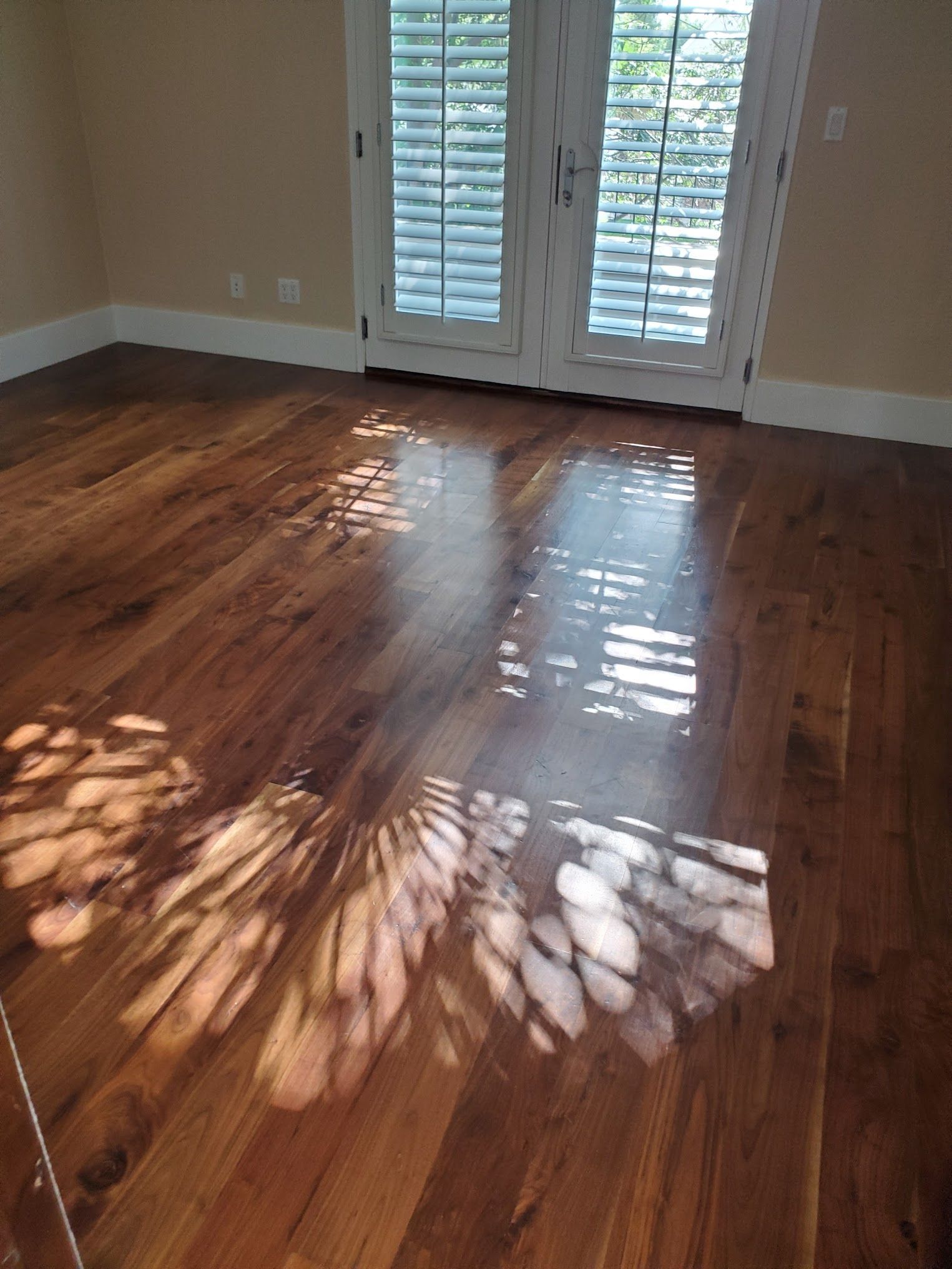 Hardwood floor with sunlight patterns, in a room with shuttered doors.