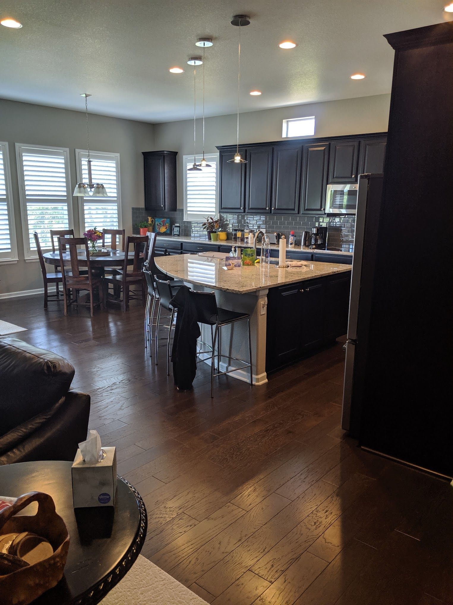Open-concept kitchen with dark cabinets and island, dining area with table and chairs, hardwood floors.