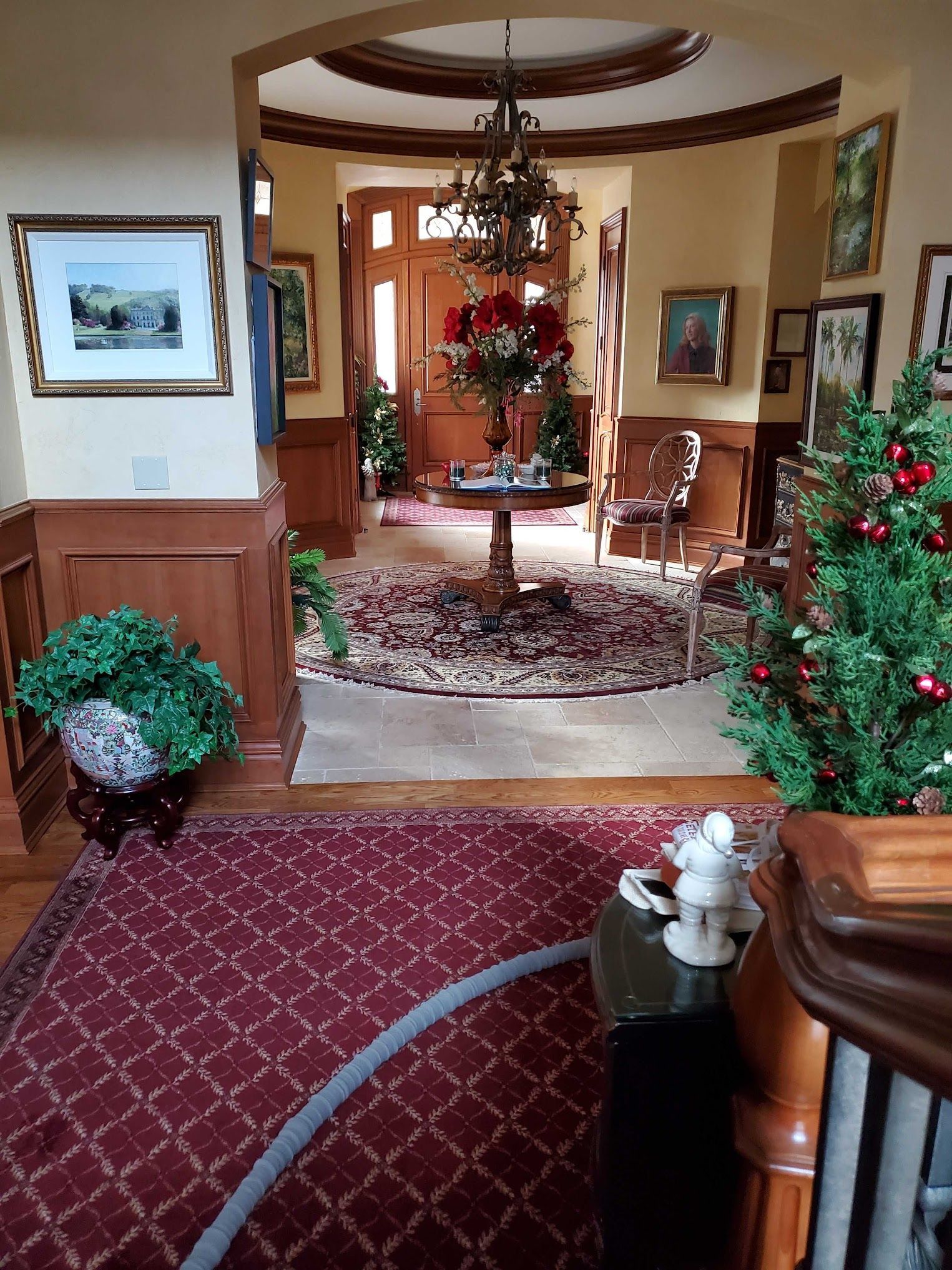 A hallway entrance with a rug, table, and Christmas decor; brown wood paneling and a chandelier.